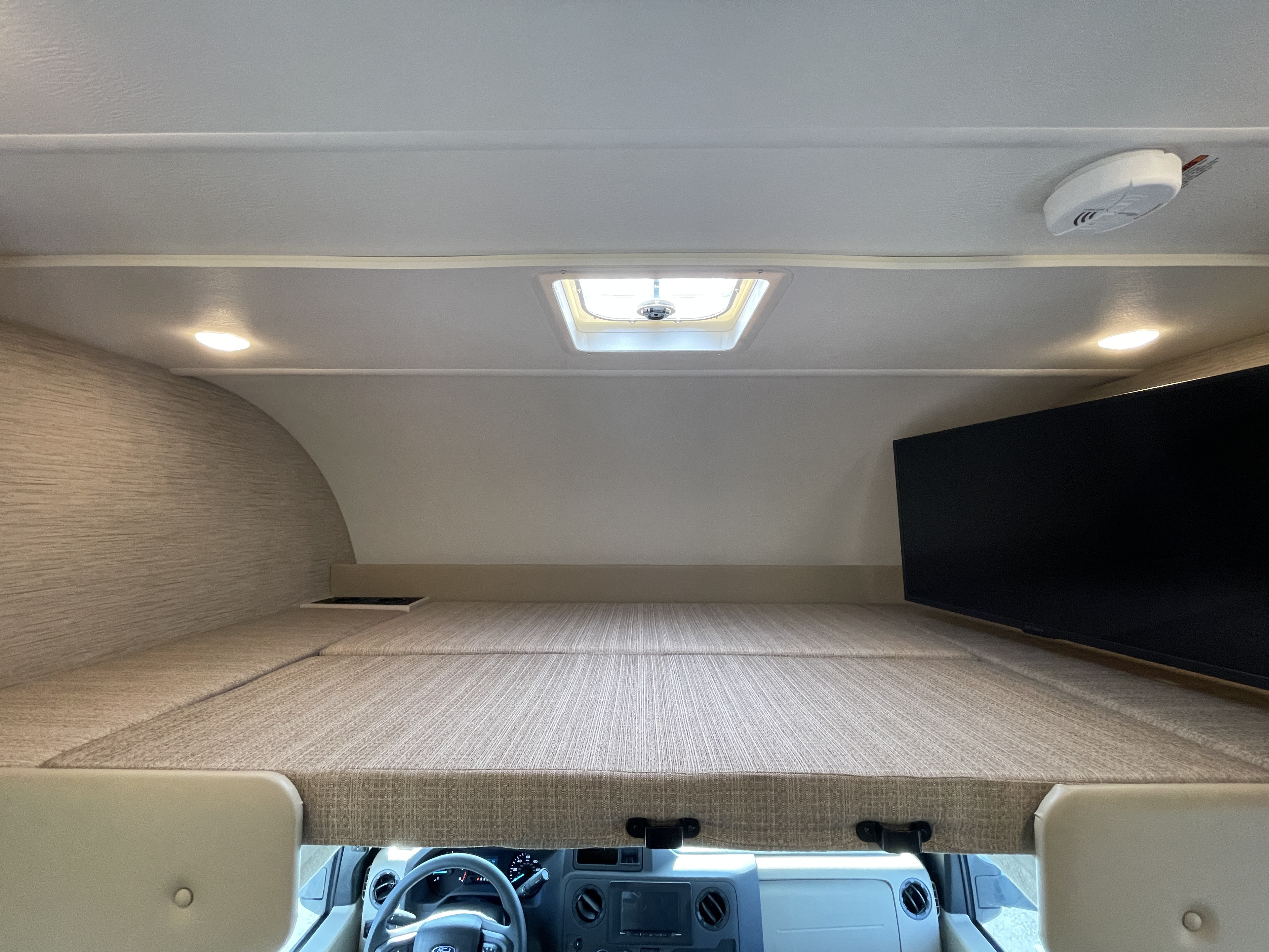 Spacious cab-over bunk and entertainment area in an RV rental, featuring a skylight, lights, and a TV.. Thor Motor Coach Four Winds 2023
