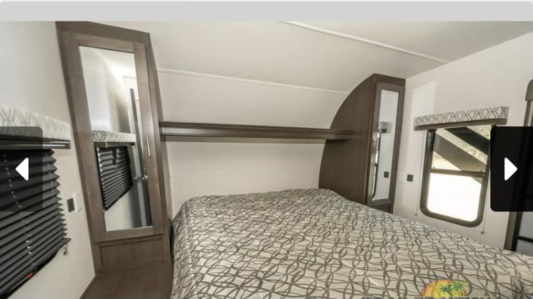 RV rental interior: A compact bedroom features a patterned bed, mirrored cabinets, an overhead shelf, and windows.. Forest River Stealth 2018