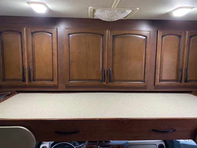 An RV rental interior: wood overhead cabinets with black handles, and a light-colored bunk bed above the cab.. Tioga Fleetwood 2011