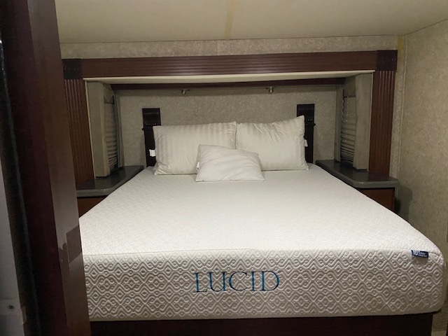 Comfortable RV rental bedroom featuring a white Lucid mattress, pillows, and built-in wood shelving. A cozy space for travel.. Tioga Fleetwood 2011