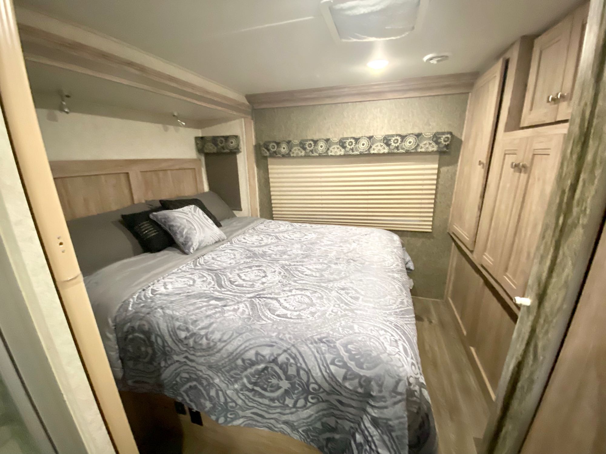 RV rental bedroom showcasing a comfortable bed with patterned comforter, wooden cabinets, and a window.. Forest River Sunseeker 2018