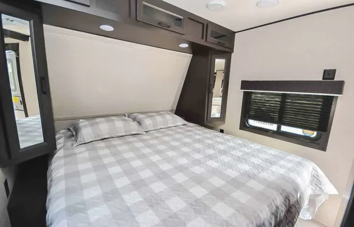 Spacious RV rental bedroom with checkered bed, overhead cabinets, and window. Perfect for your next adventure.. Jayco Jay Flight 2022