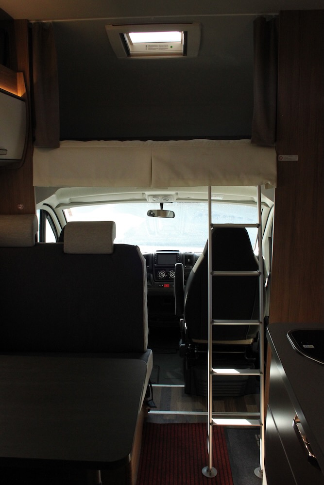 RV rental interior showcasing the over-cab bunk with ladder, front cab, seating, and compact kitchen.. Weinsberg 700DG 2022