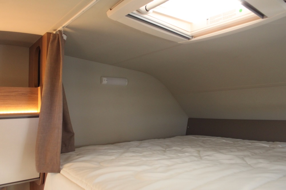 A cozy RV rental sleeping area features a comfortable bed, overhead skylight, and reading light, ready for travel adventures.. Weinsberg 700DG 2022