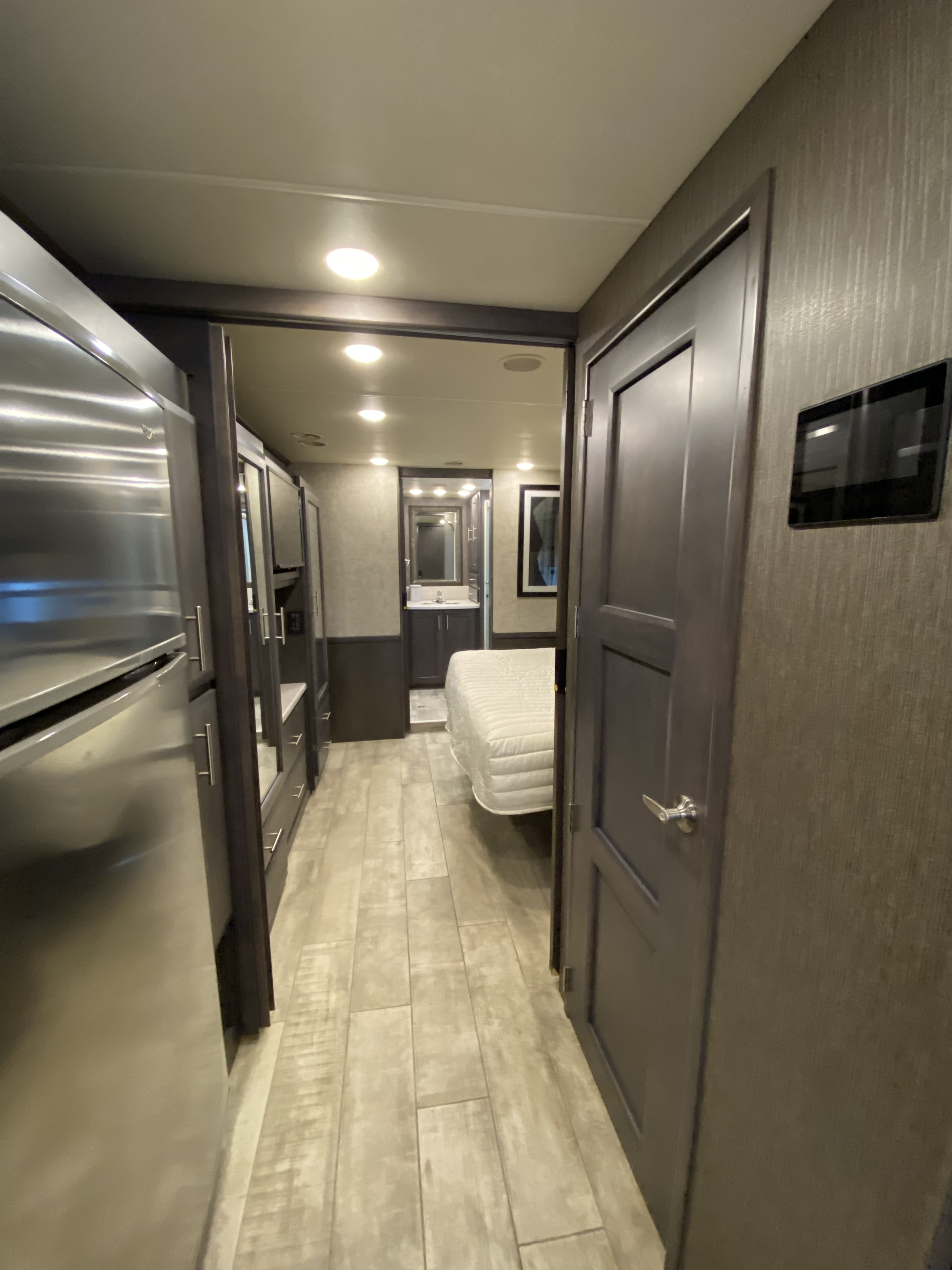 Modern rv rental interior featuring kitchen appliances, a hallway leading to a bedroom with a visible bed, and a bathroom vanity.. Thor Aria 2020