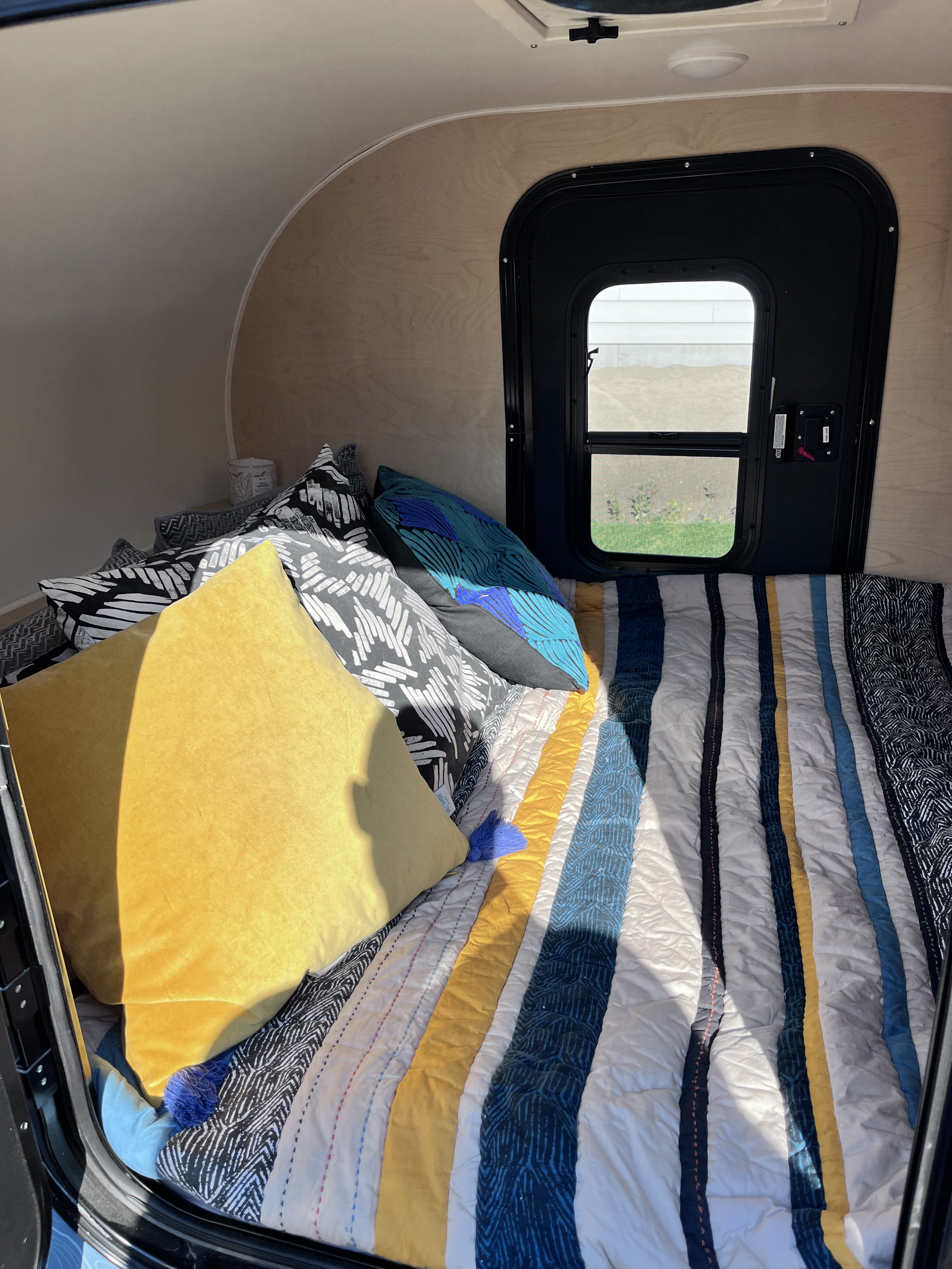 Cozy RV rental interior: bed with colorful pillows & striped comforter, sunlight from window.. modern buggy Little Buggy 2022