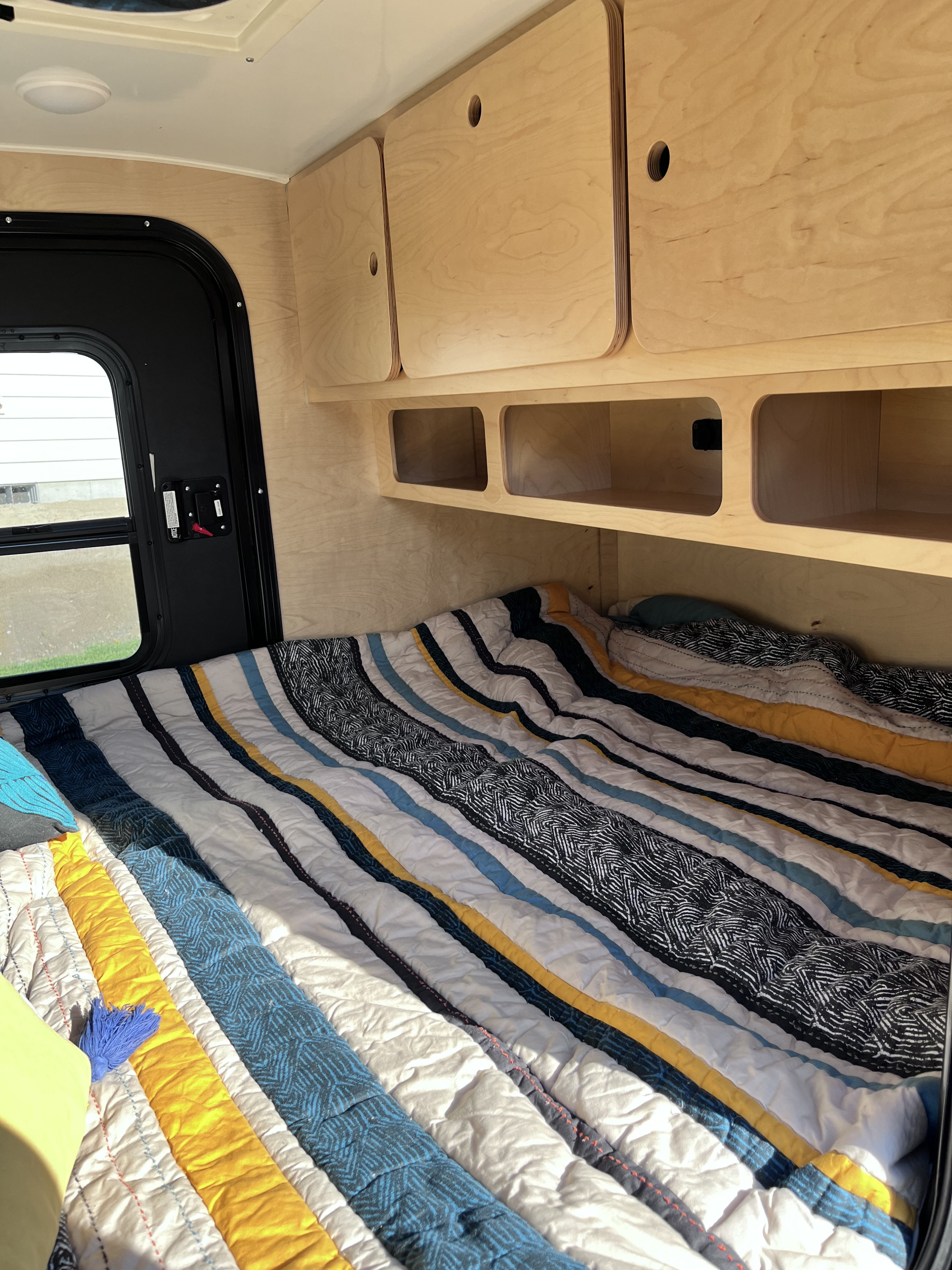 Inside an RV rental: Bed with colorful striped quilt, light wood overhead cabinets, and built-in storage.. modern buggy Little Buggy 2022