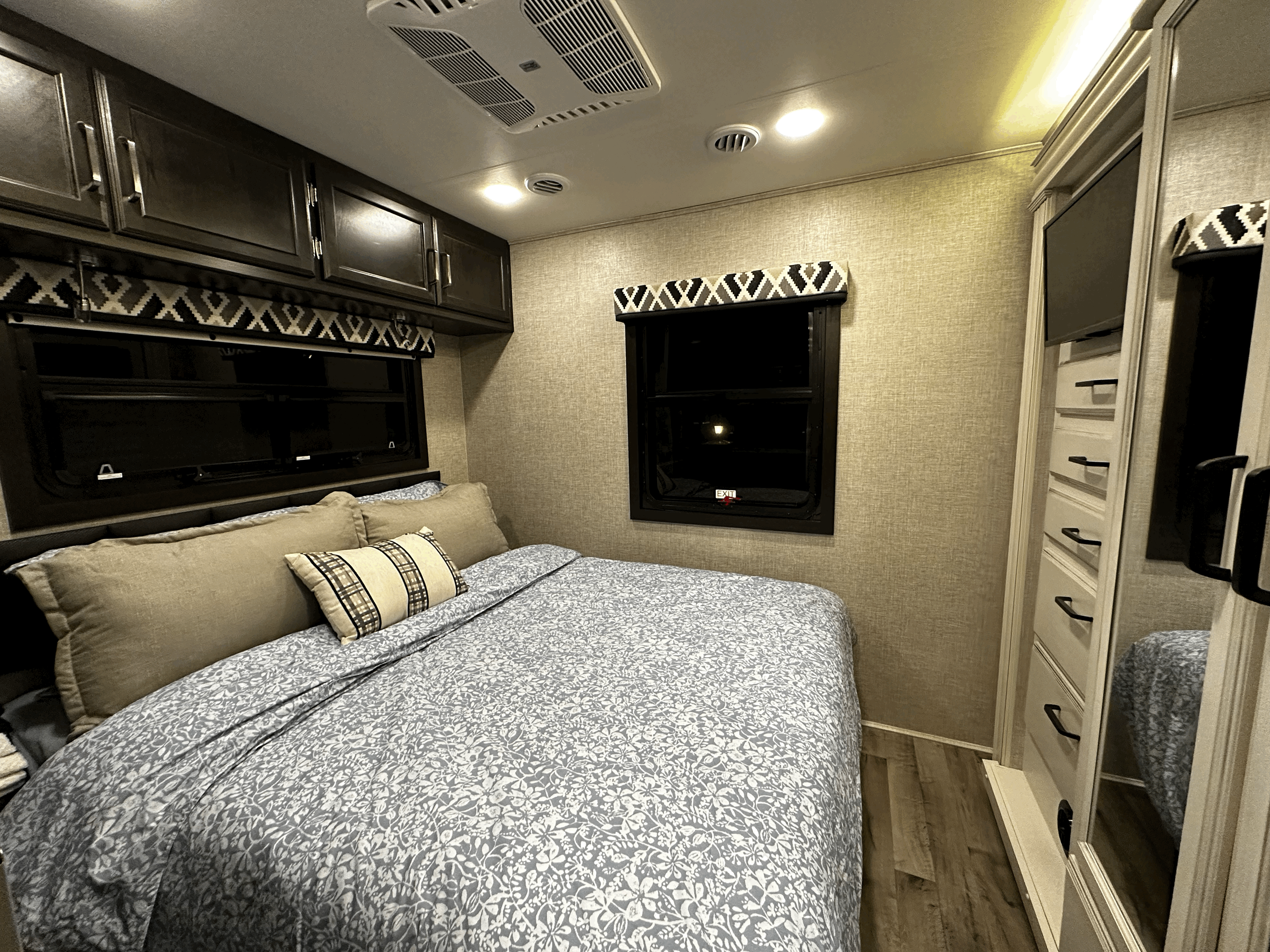 Cozy rv rental bedroom: floral bed, dark cabinets, two windows, mirrored dresser, and ceiling AC/lights visible.. Joyco alante 29f 2022