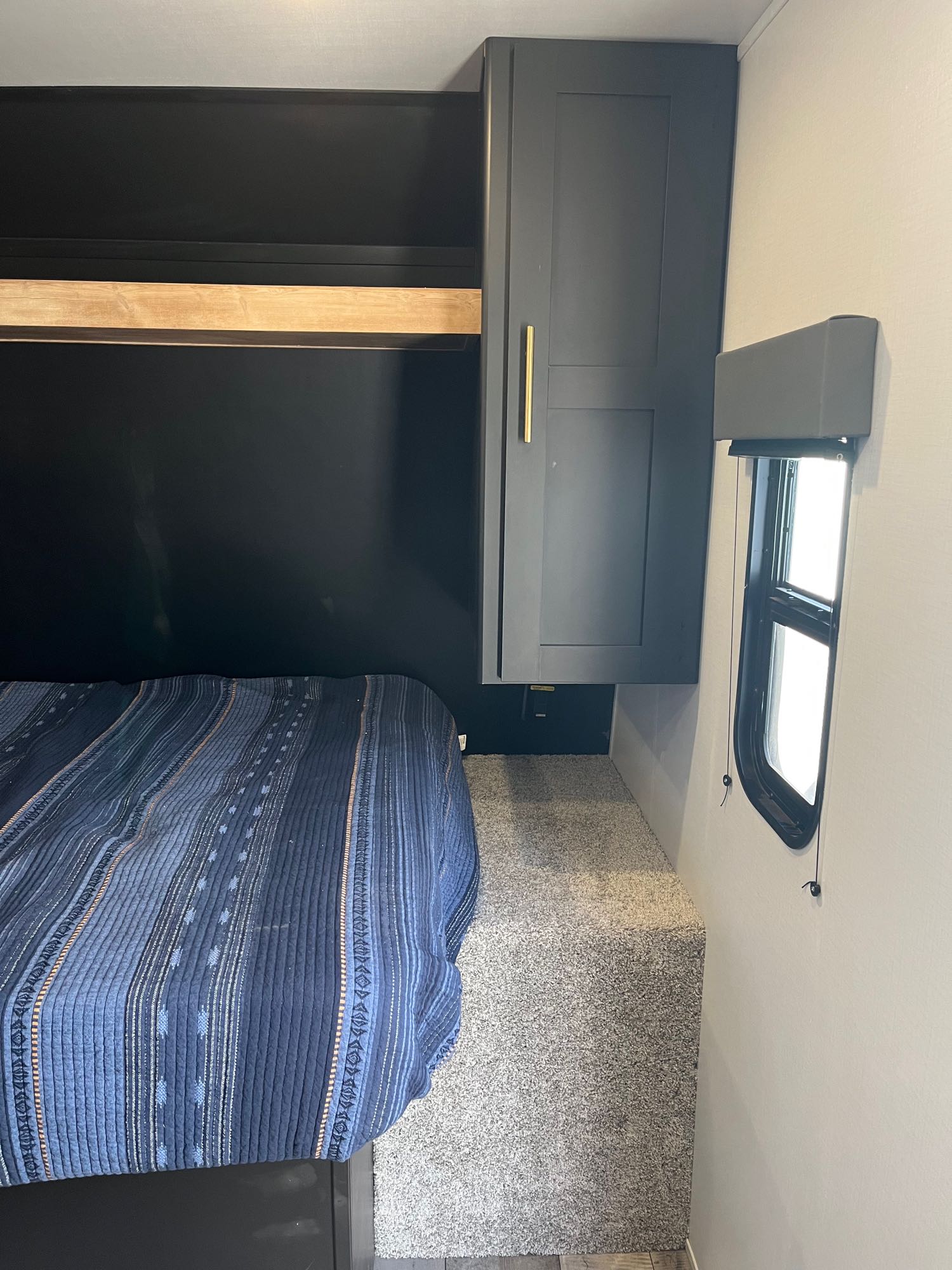 Comfortable rv rental bedroom with a blue bed, wood shelf, gray cabinet, and small window.. Keystone RV Springdale 2022