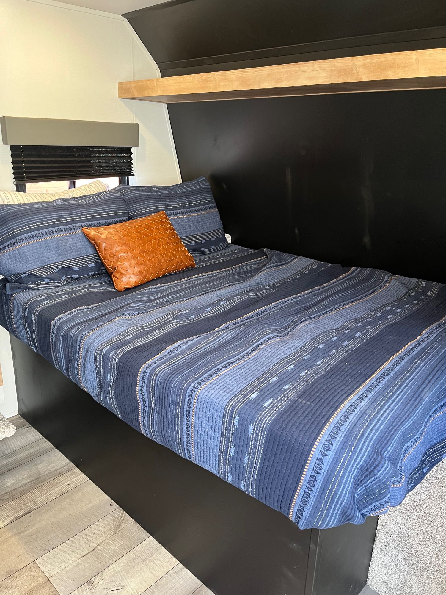 Inside this RV rental, a modern bedroom features blue bedding, a woven orange pillow, and light wood shelf.. Keystone RV Springdale 2022