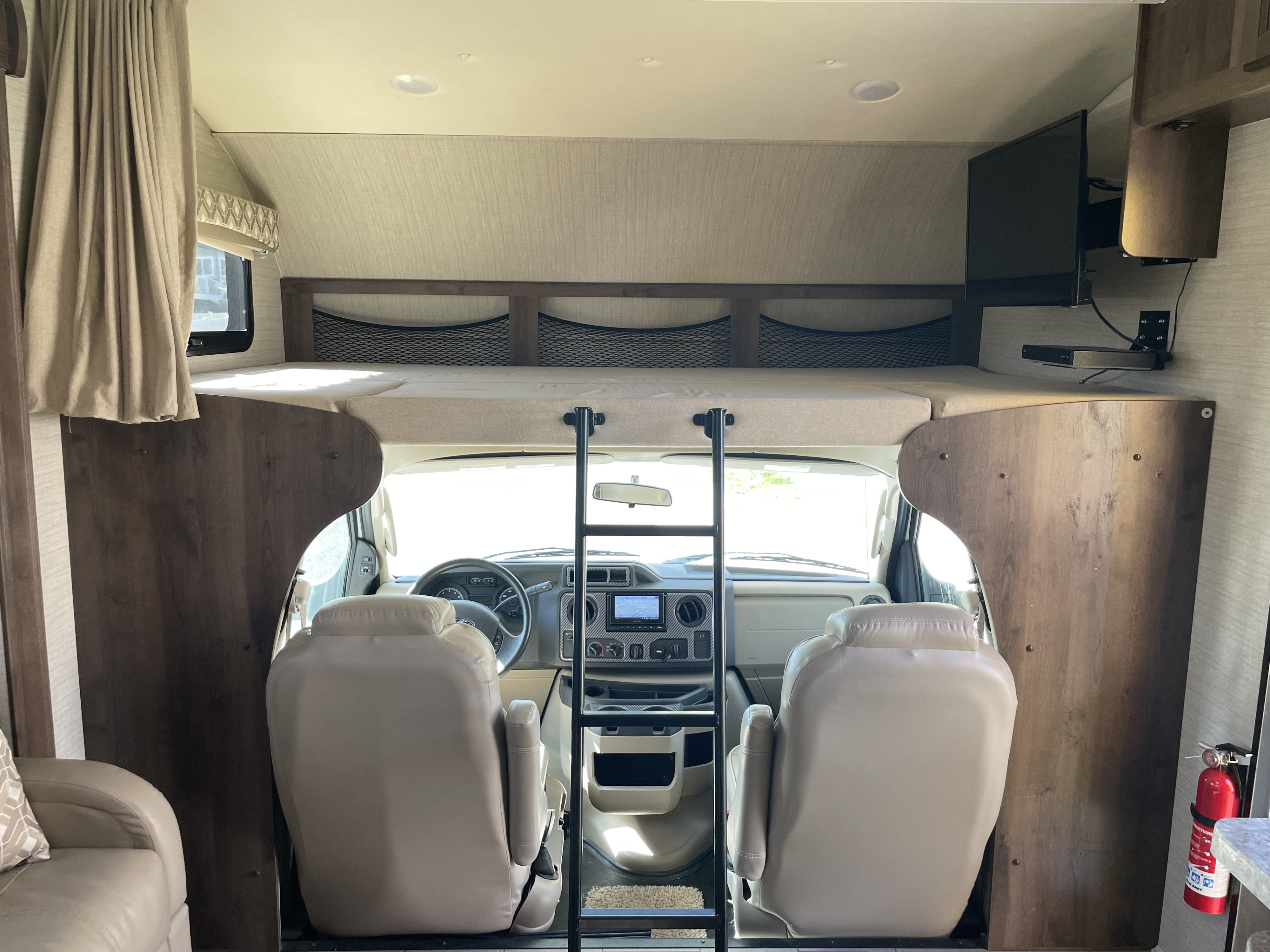 This RV rental interior shows the front cabin, an overhead bunk with ladder access, and a wall-mounted TV for onboard comfort.. Jayco Greyhawk 2018