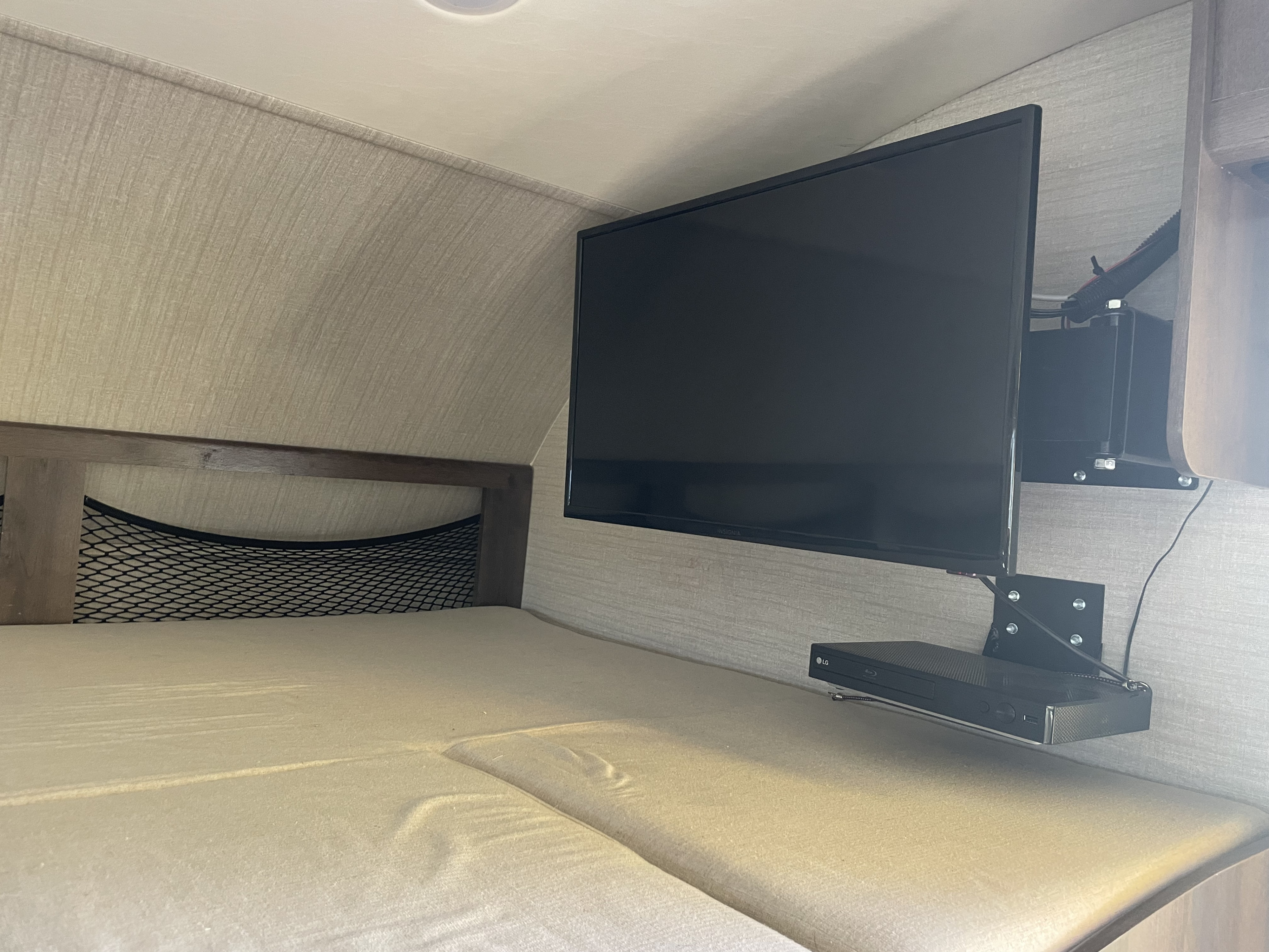 Cozy RV rental bedroom with a comfy bed, wall-mounted TV & LG Blu-ray player, plus mesh storage netting. Perfect for travel entertainment.. Jayco Greyhawk 2018