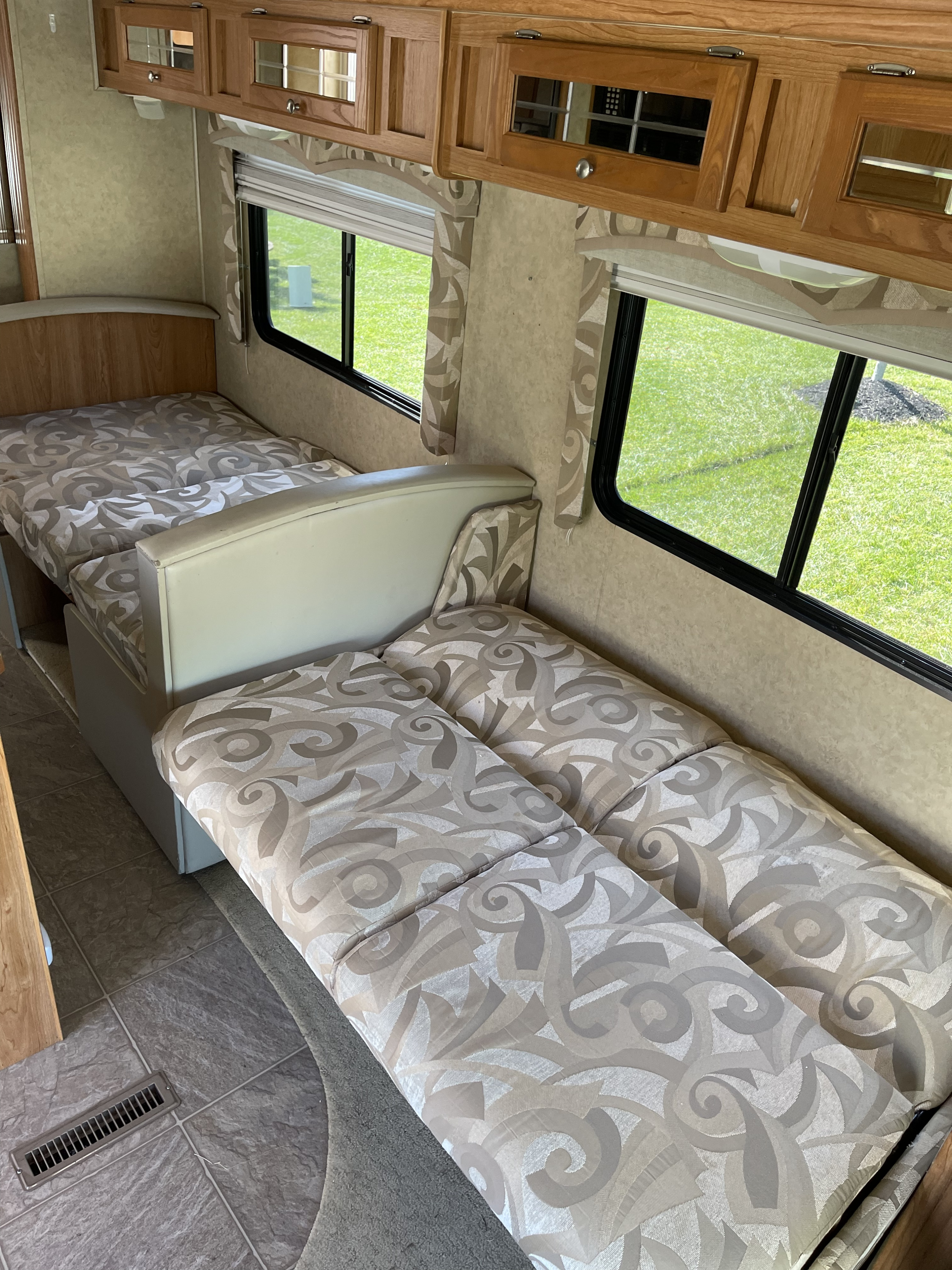 Interior view of an RV rental with patterned convertible seating/bed, wooden overhead cabinets, and large windows.. Holiday Rambler Atlantis 2007
