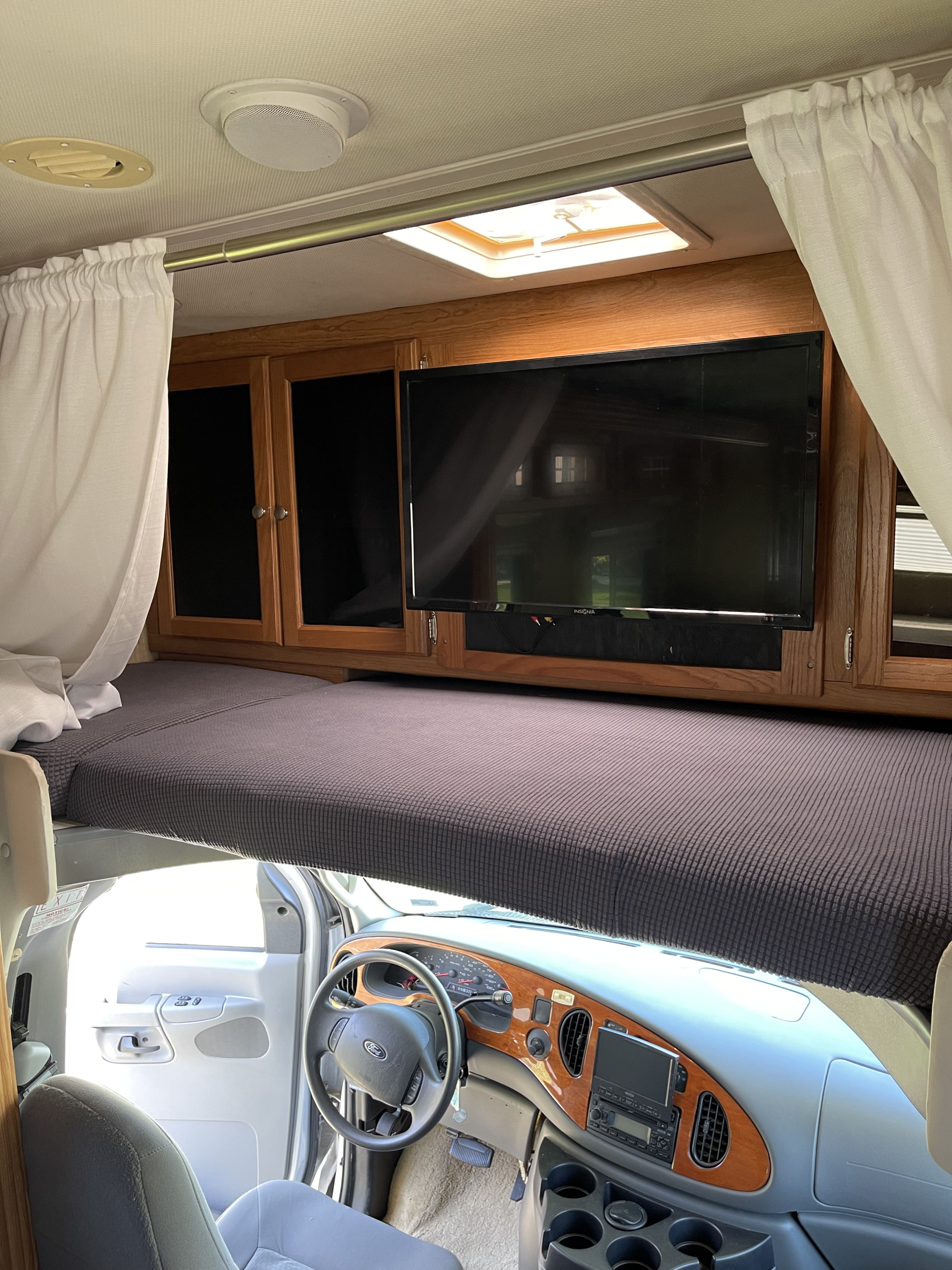 Inside an RV rental: cozy cab-over bed with TV, plus the spacious driver's cockpit with steering wheel and dashboard.. Holiday Rambler Atlantis 2007