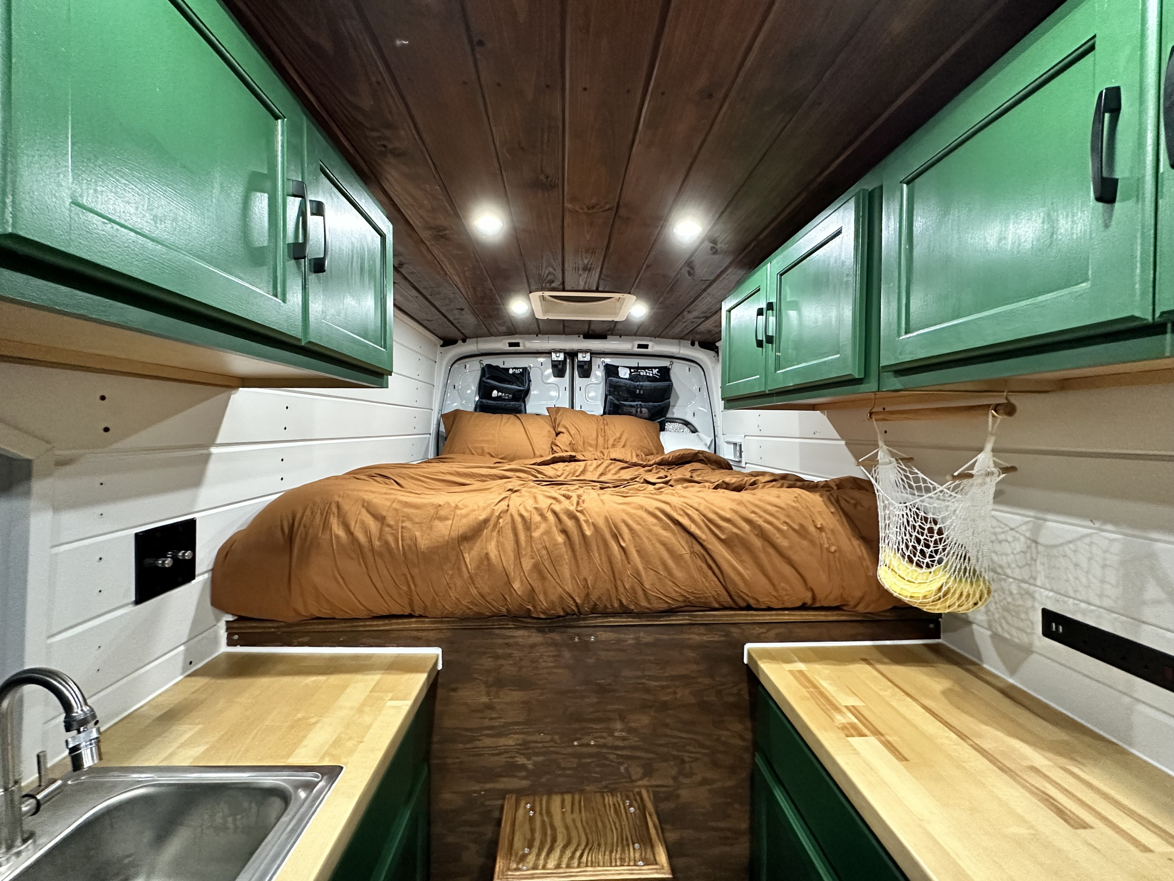 Cozy camper van RV rental interior with a bed, green cabinets, wood ceiling, and compact kitchen.. Ford Transit 2015
