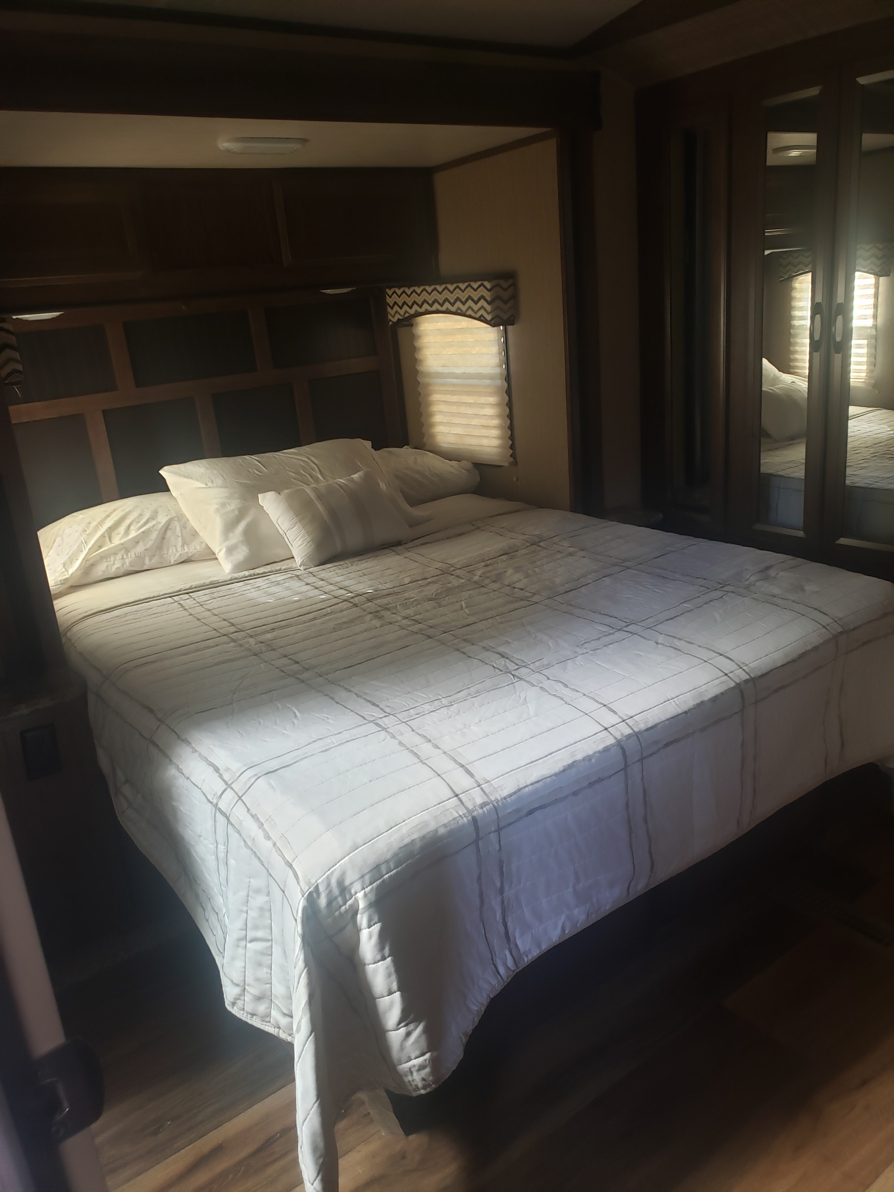 Sunlit RV rental bedroom with a neatly made bed, patterned blinds, built-in storage, and mirrored wardrobe.. Cruiser RV Radiance Touring 2016