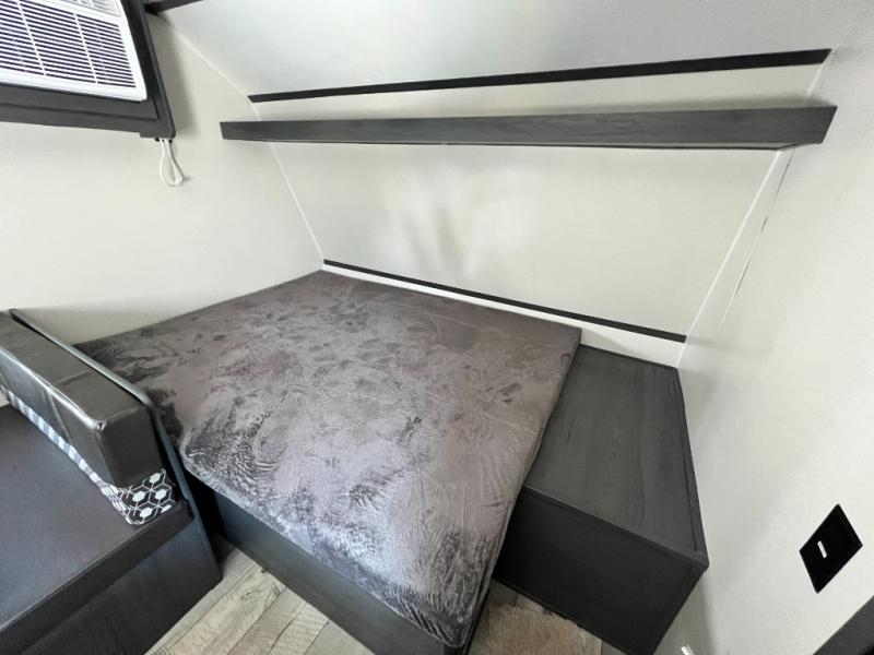 Inside an rv rental, a compact sleeping area with a gray bed, a black dinette bench, and an AC unit.. Aspen Trail LE 2022