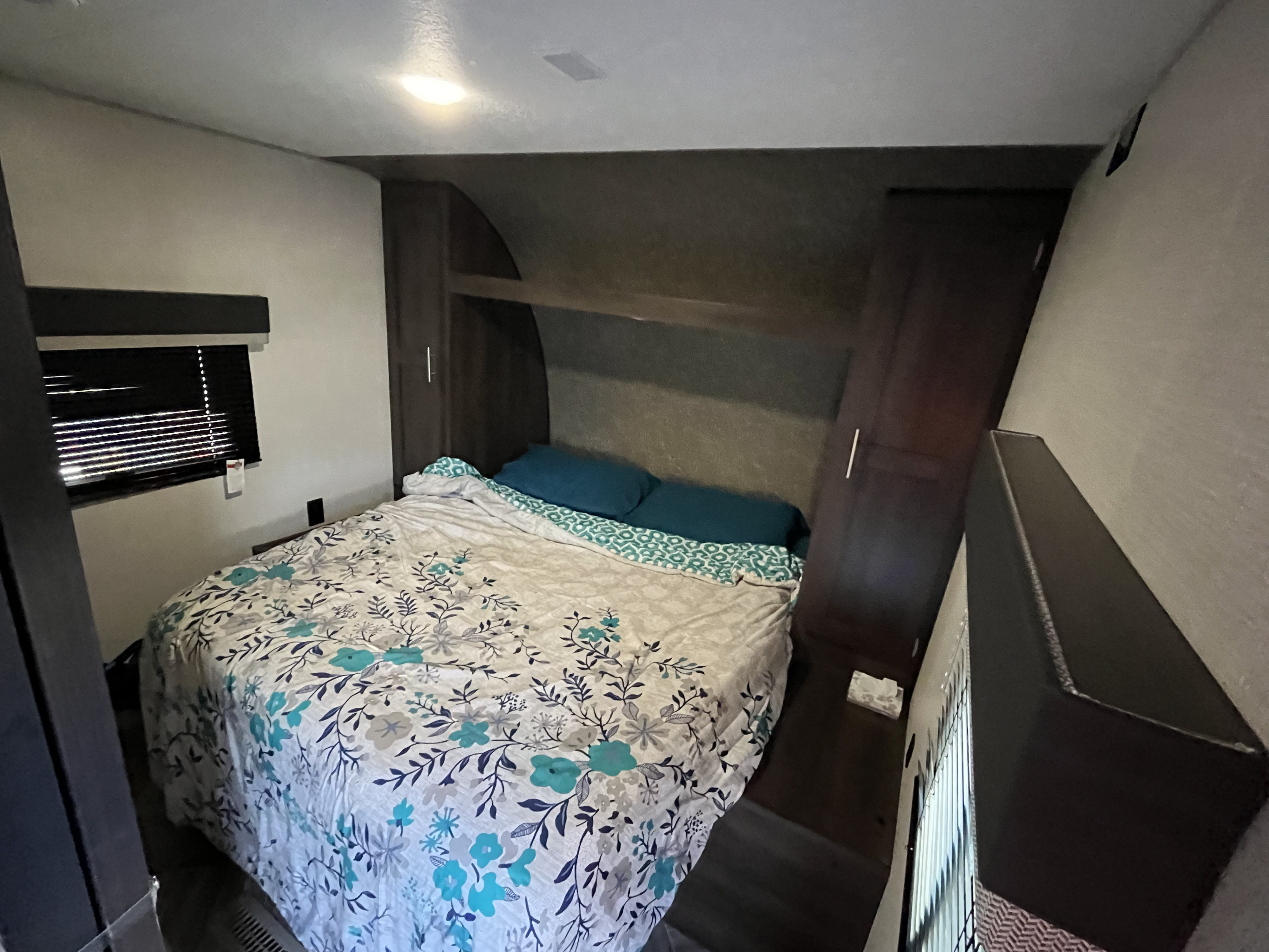 Cozy RV rental bedroom featuring a floral bedspread, window blinds, and built-in storage.. K-Z Manufacturing Sportsmen 2021