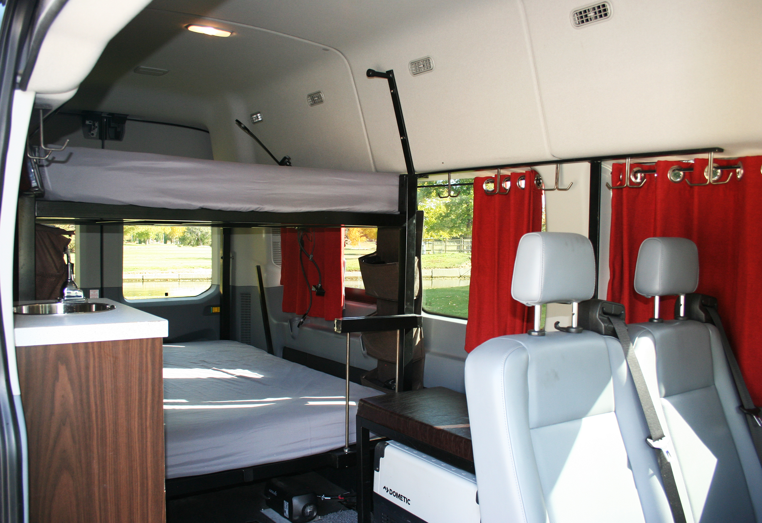 RV rental: Cozy camper interior with bunk beds, sink, seats, and red curtains, offering a home-like travel experience.. Ford Transit 2022
