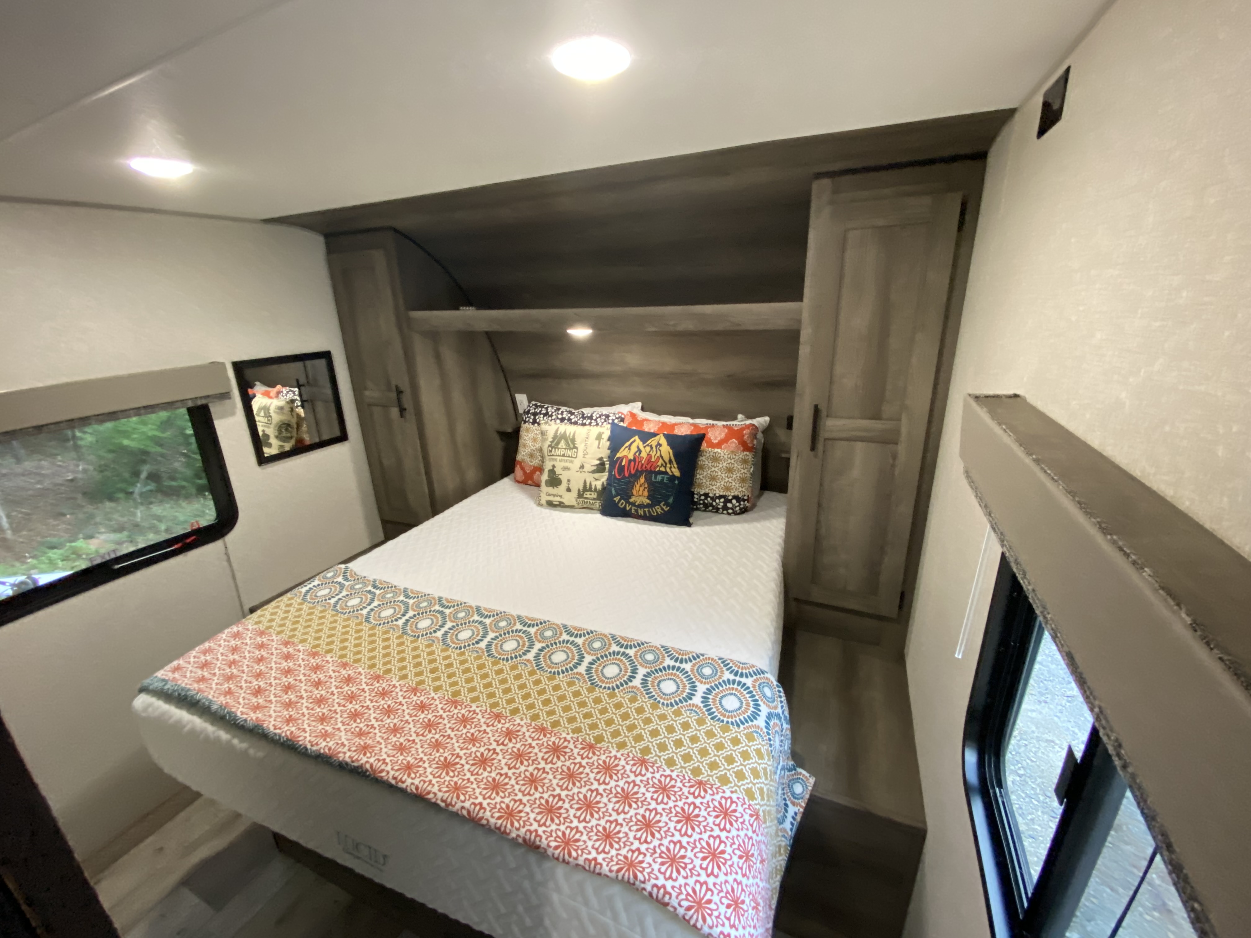 Inside a comfy RV rental: a neat bedroom featuring a bed, colorful pillows, and ample storage.. Sportsmen SE 2021