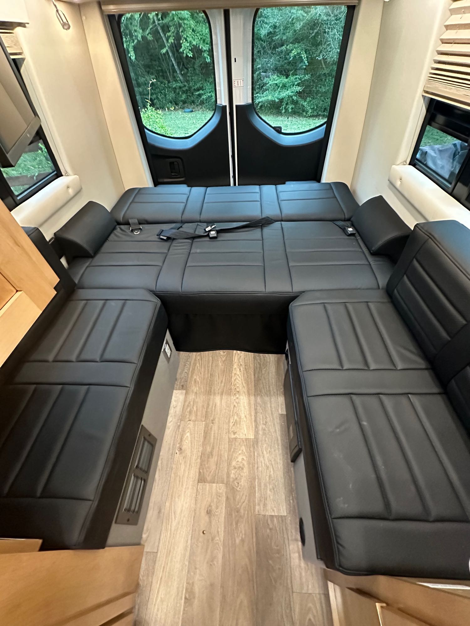 RV rental interior shows black cushioned convertible seating/bed, wood floor, and rear windows with greenery outside.. Coachmen Other 2022