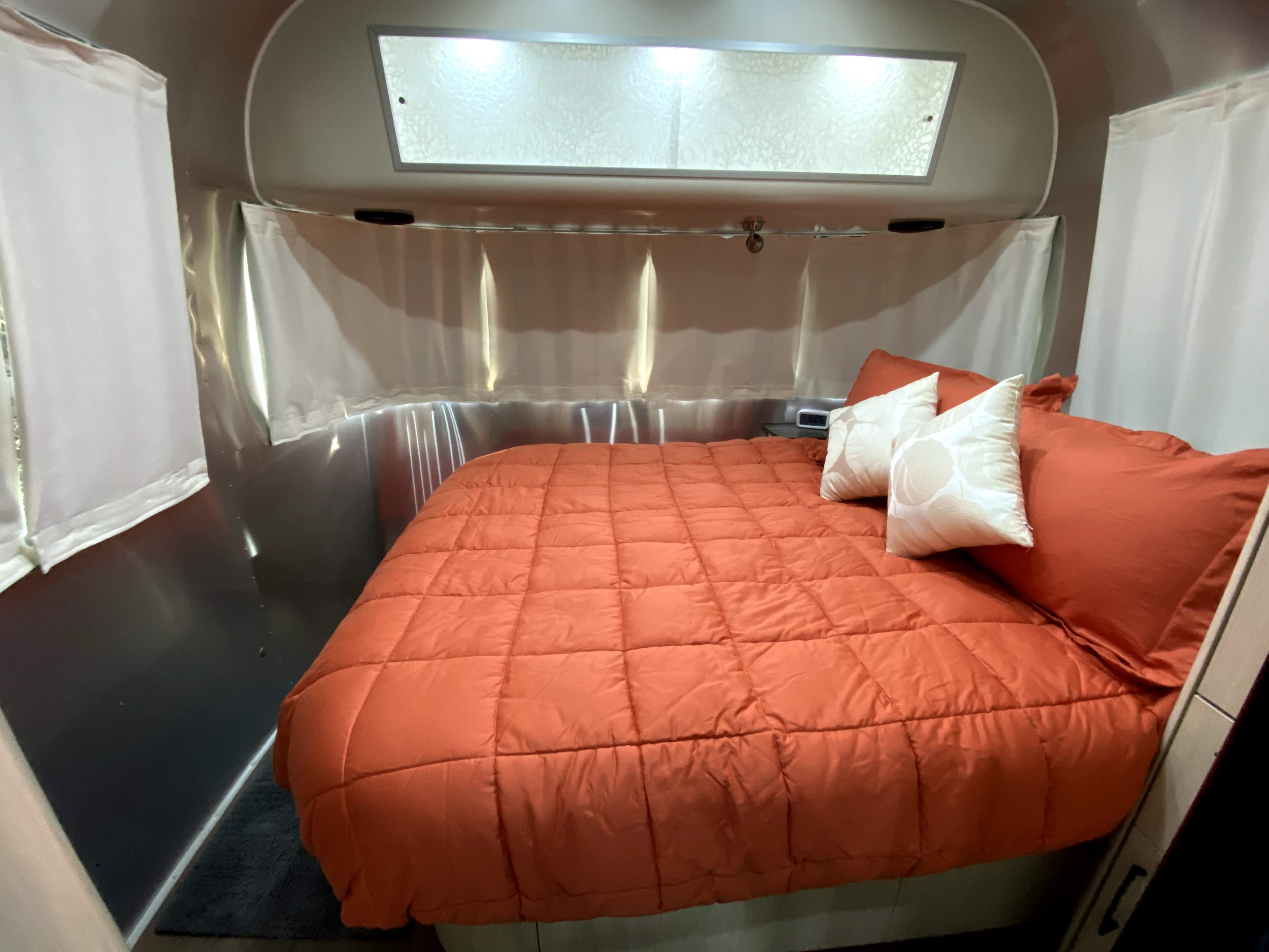 Step into comfort: a cozy RV rental bedroom with a large orange bed, white curtains, and sleek silver walls.. Airstream International 2017