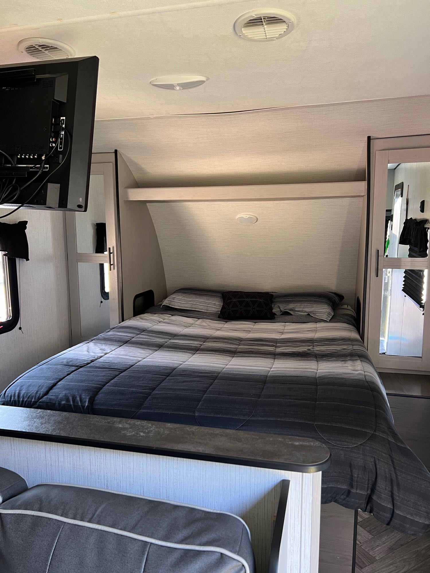 RV rental bedroom with bed, wall-mounted TV, and storage, offering compact comfort for travelers.. Heartland Prowler 2021