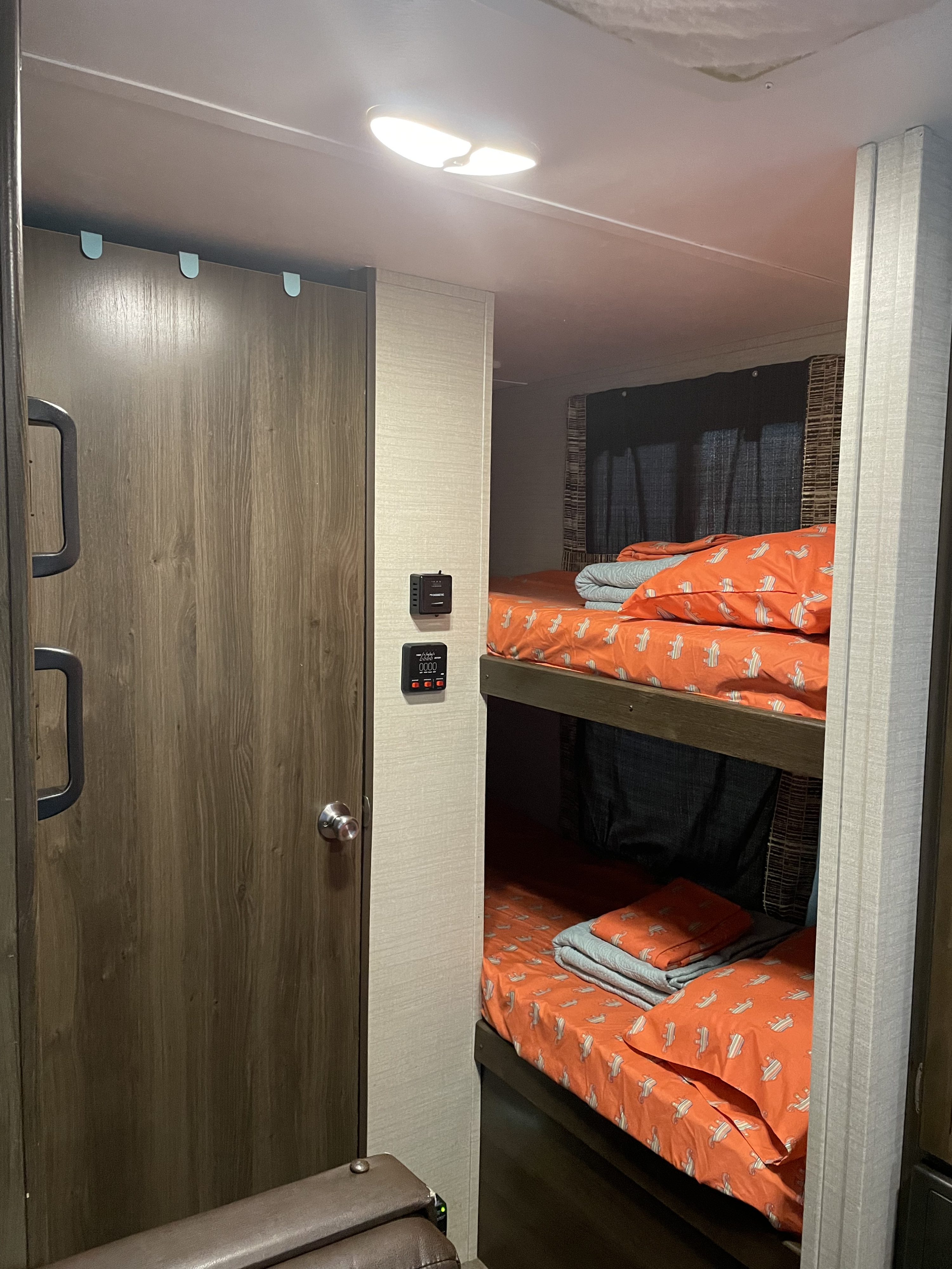 RV rental interior featuring bunk beds with vibrant orange sheets, a wood-paneled door, and environmental controls.. Keystone Bullet 2018