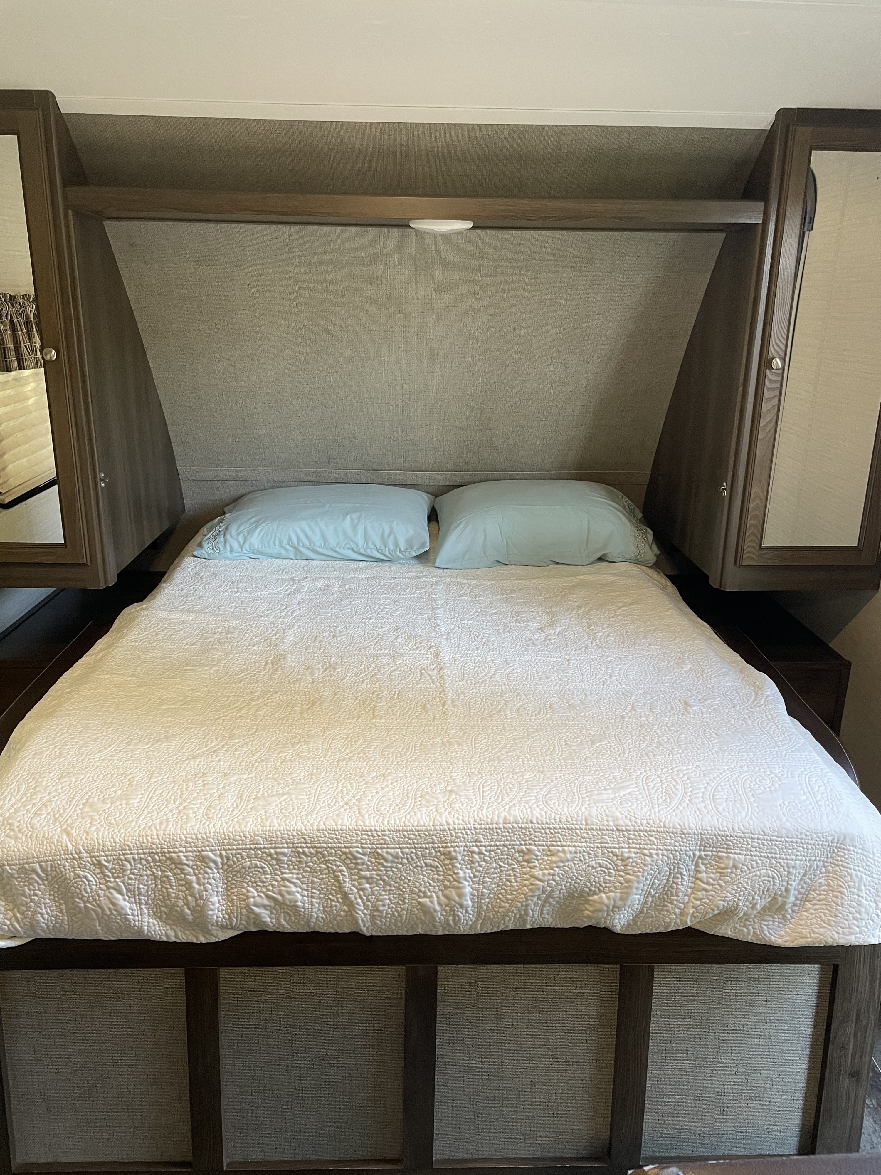 Cozy RV rental bedroom with a neatly made bed, light blue pillows, overhead storage, and side cabinets. Ideal for travel.. Keystone Bullet 2018