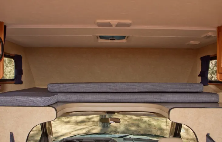 Inside an RV rental: view of the comfortable over-cab bed area with striped cushions, side windows, and ceiling vent.. Thor Majestic 2015