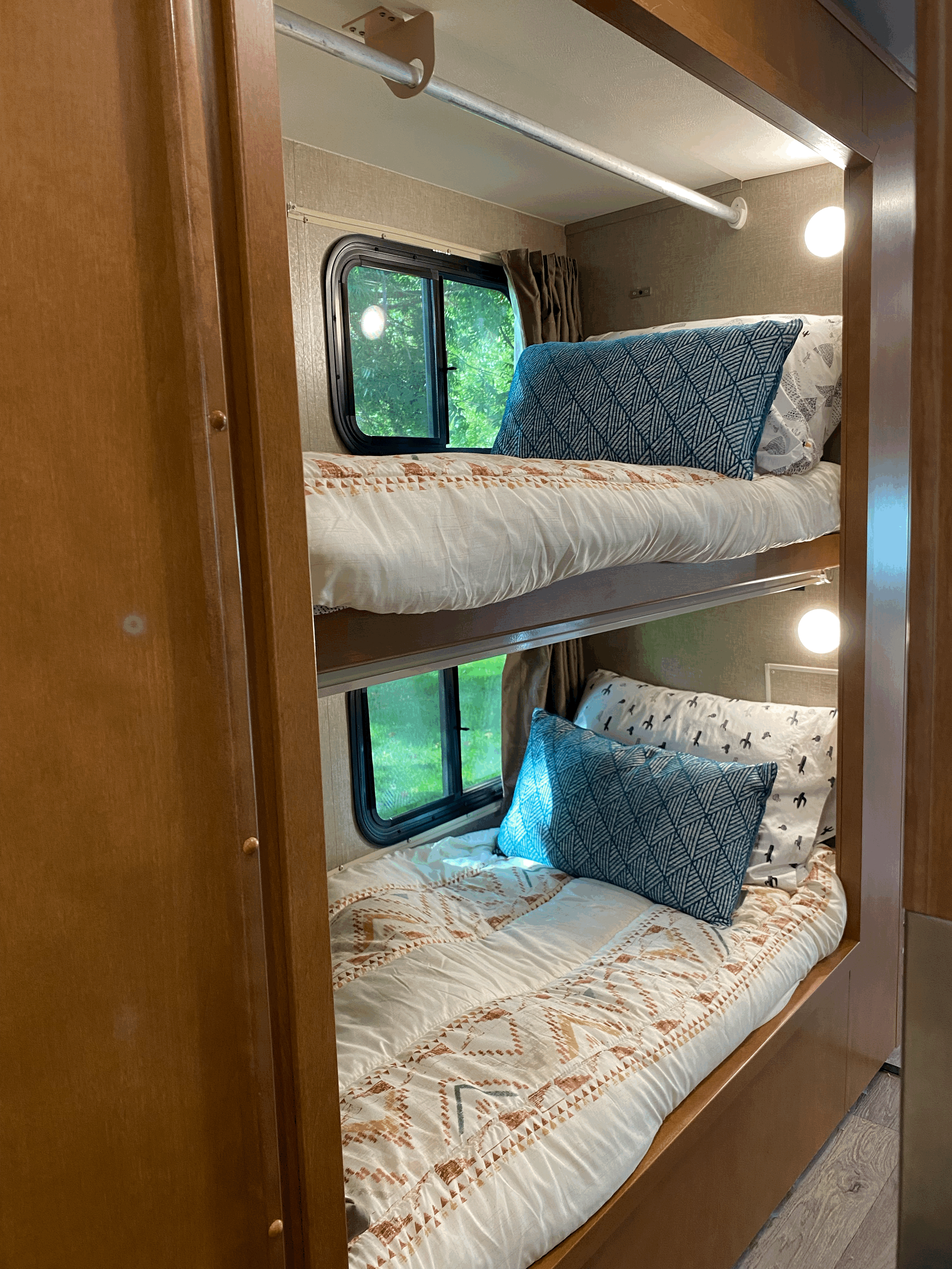 View inside an RV rental showing two neatly made bunk beds with pillows, windows, and individual reading lights.. Winnebago Minnie Winnie 2019