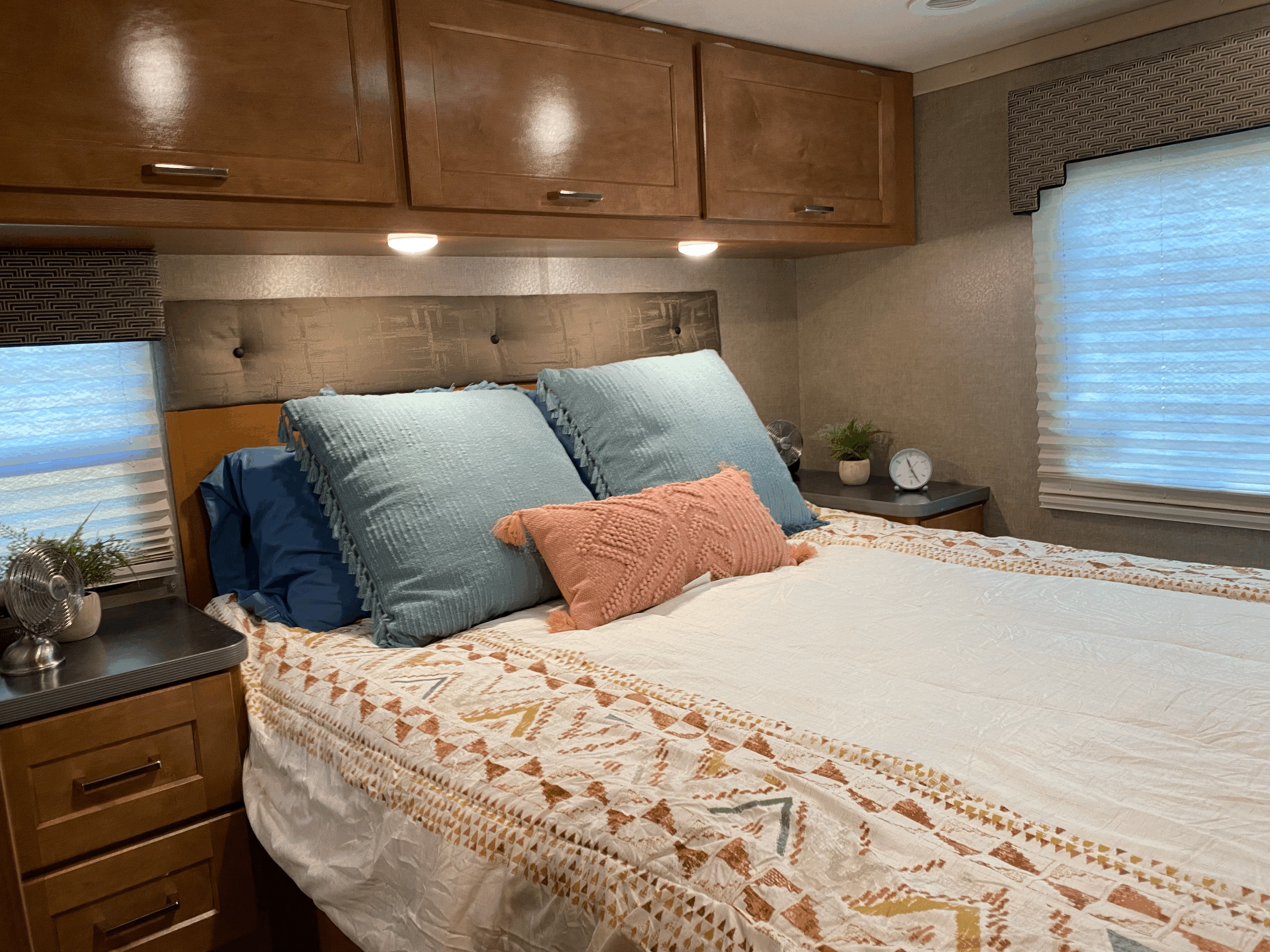 Cozy RV rental bedroom featuring a comfortable bed with patterned bedding, overhead cabinets, and compact nightstands.. Winnebago Minnie Winnie 2019