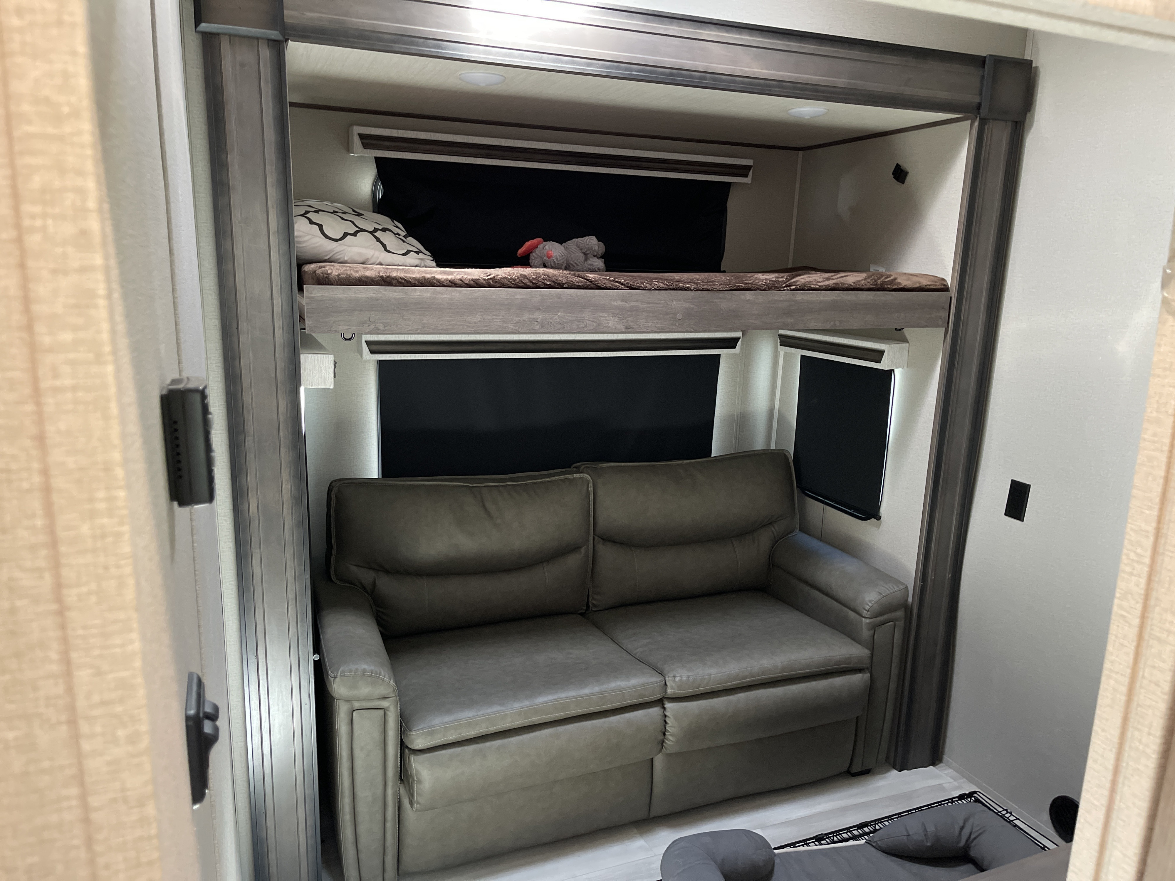 This RV rental bunkhouse features a comfy sofa and an upper bunk bed with a stuffed animal, offering flexible sleeping.. Grand Design Solitude 2021