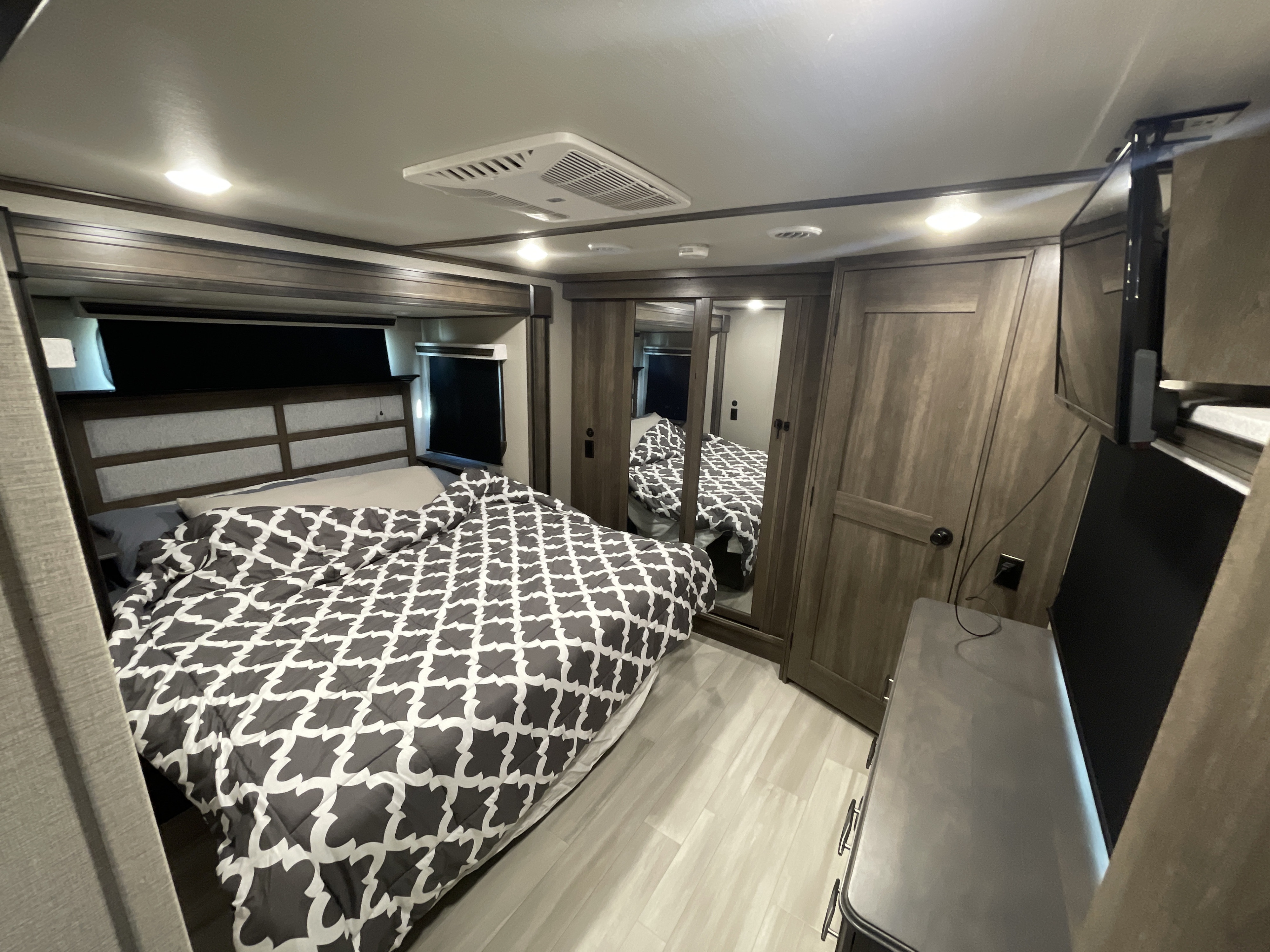 Inside an RV rental: a cozy and well-equipped bedroom with built-in storage, a comfy bed, and entertainment.. Grand Design Solitude 2021