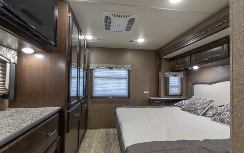 Spacious RV rental bedroom featuring a large bed, TV, and built-in storage for a comfortable journey.. Thor Hurricane 2017