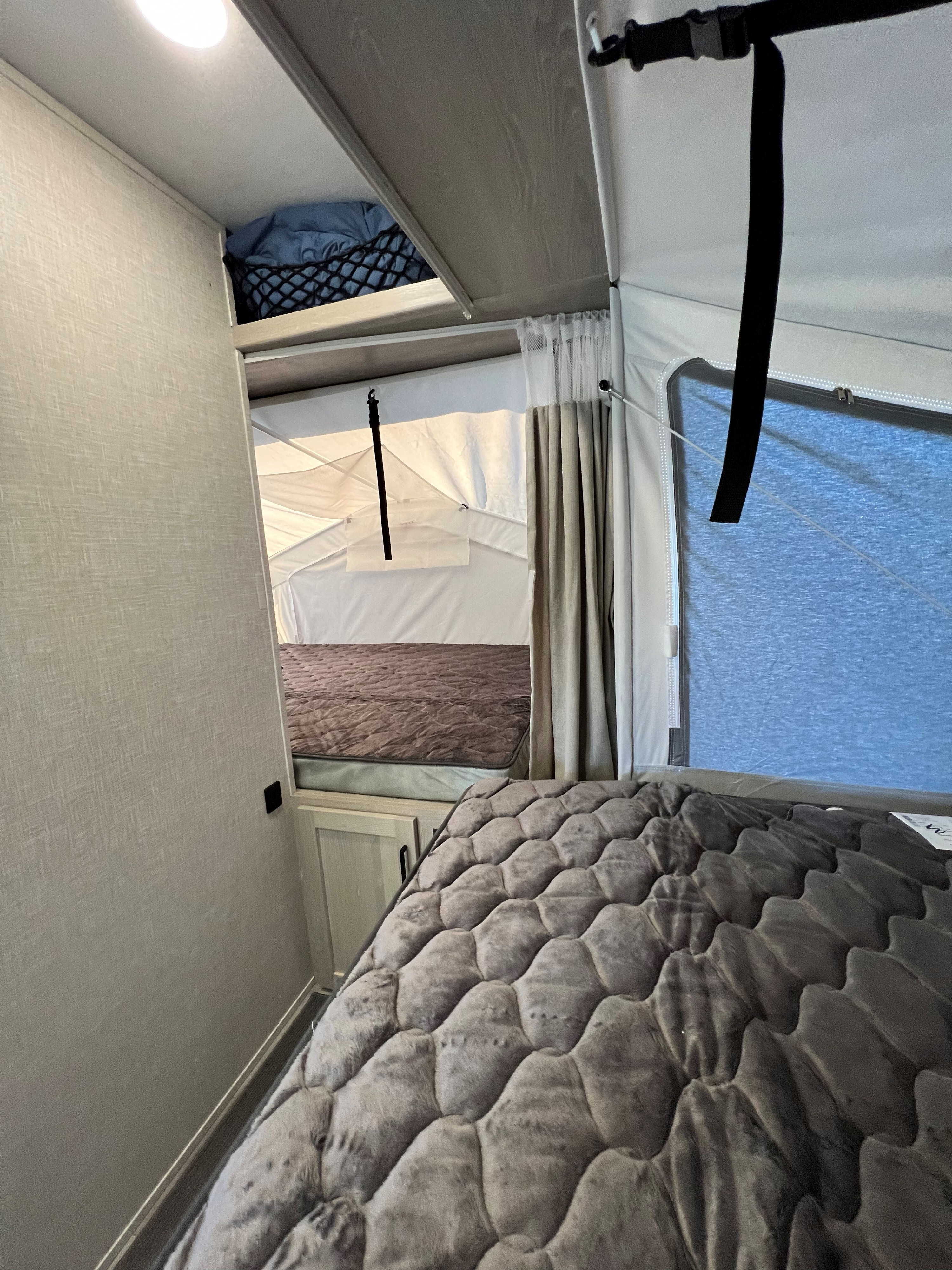 Inside an RV rental: a cozy bedroom setup with two beds, one in a pop-up tent extension and overhead storage.. Forest River Rockwood Roo 2022