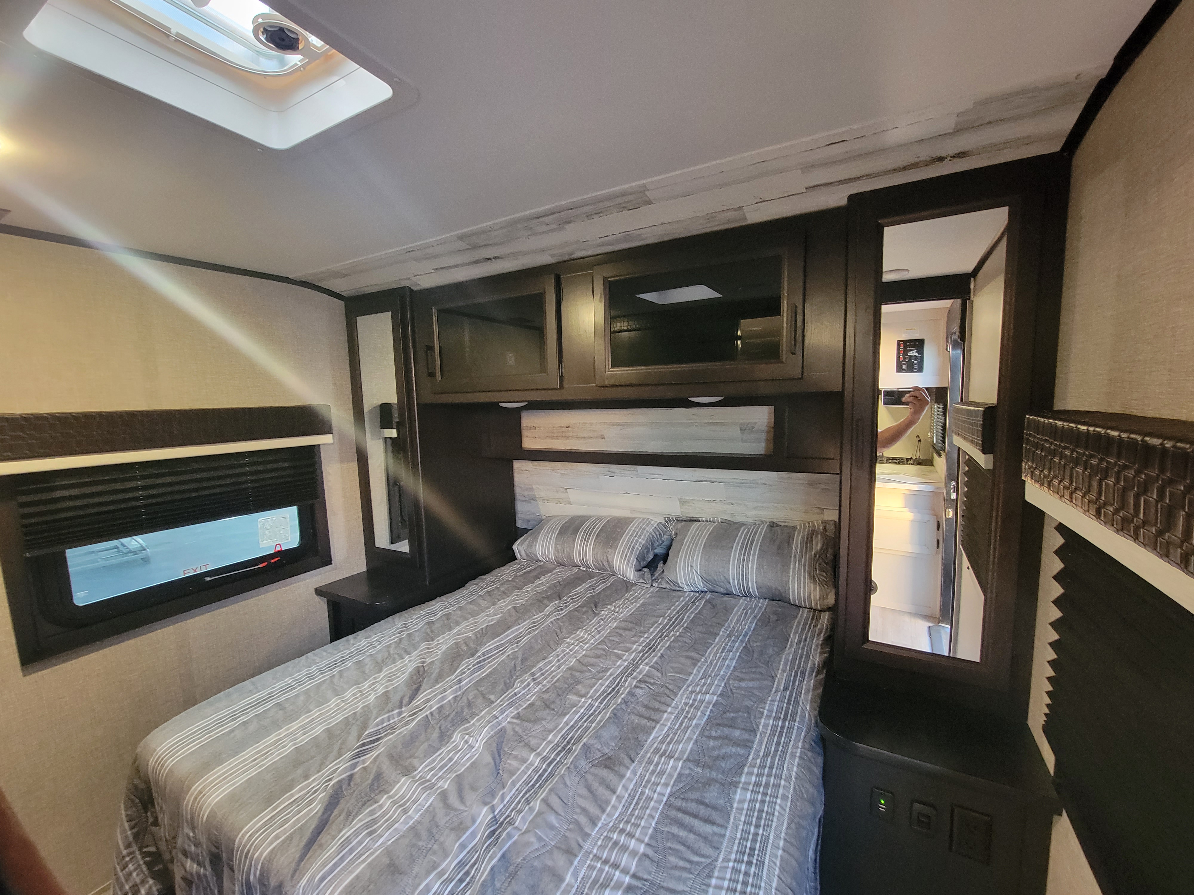 Cozy RV rental bedroom featuring a striped bed, ample overhead storage, window, and skylight for a comfortable journey.. Jayco Jay Feather 2022