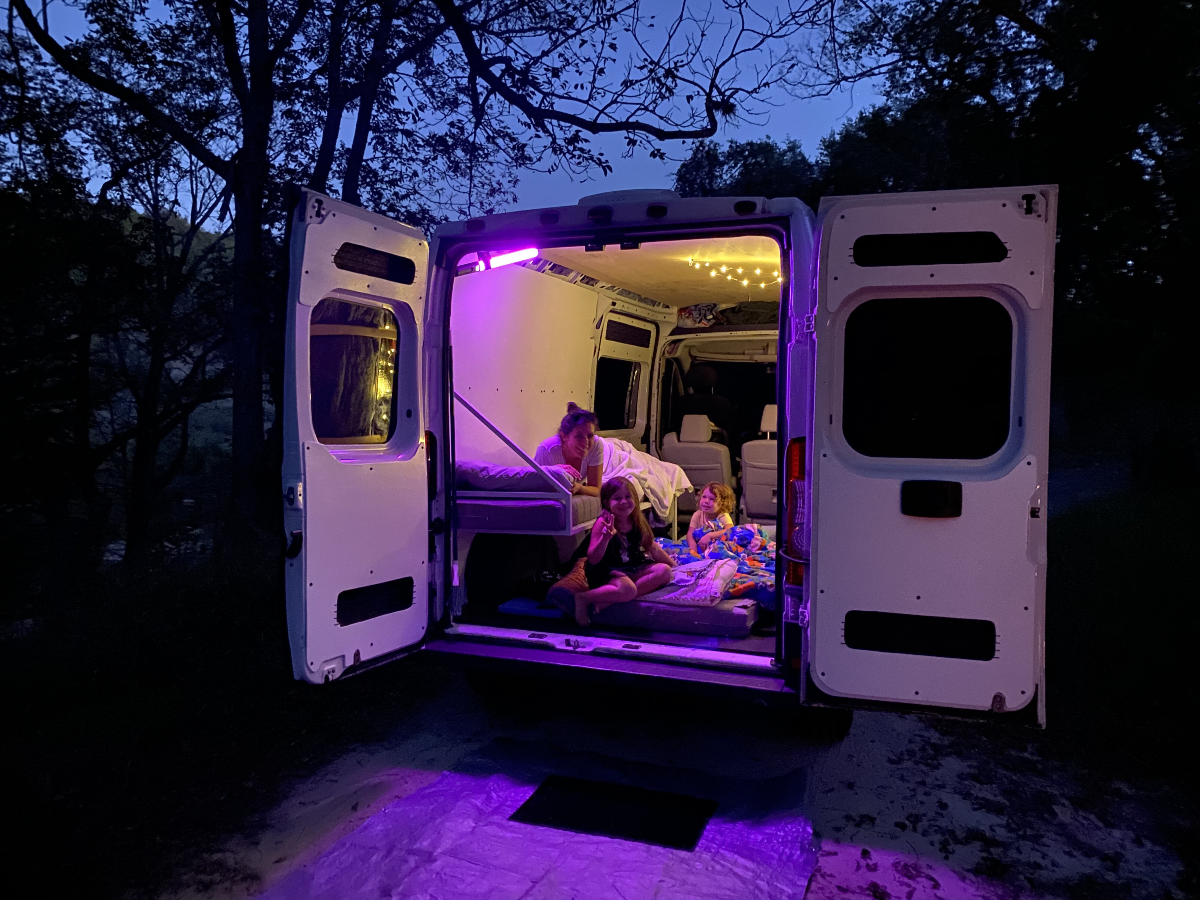 Family enjoying a cozy evening in their RV rental. Mom and kids relax inside the brightly lit camper van.. Dodge Promaster Tall 159in wheelbase 2015