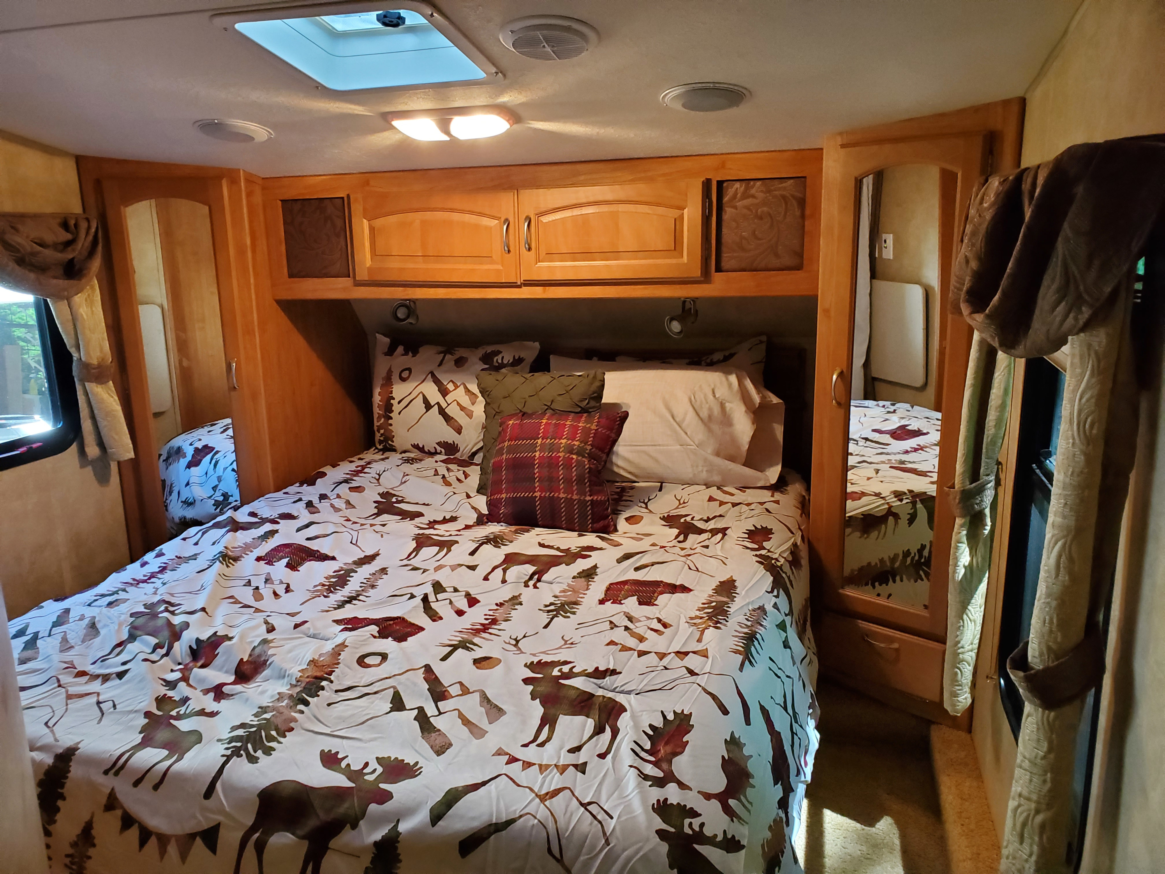 Cozy RV bedroom interior featuring a bed with nature-themed bedding, wood cabinets, and a skylight, perfect for an rv rental.. Forest River Wildcat 2009