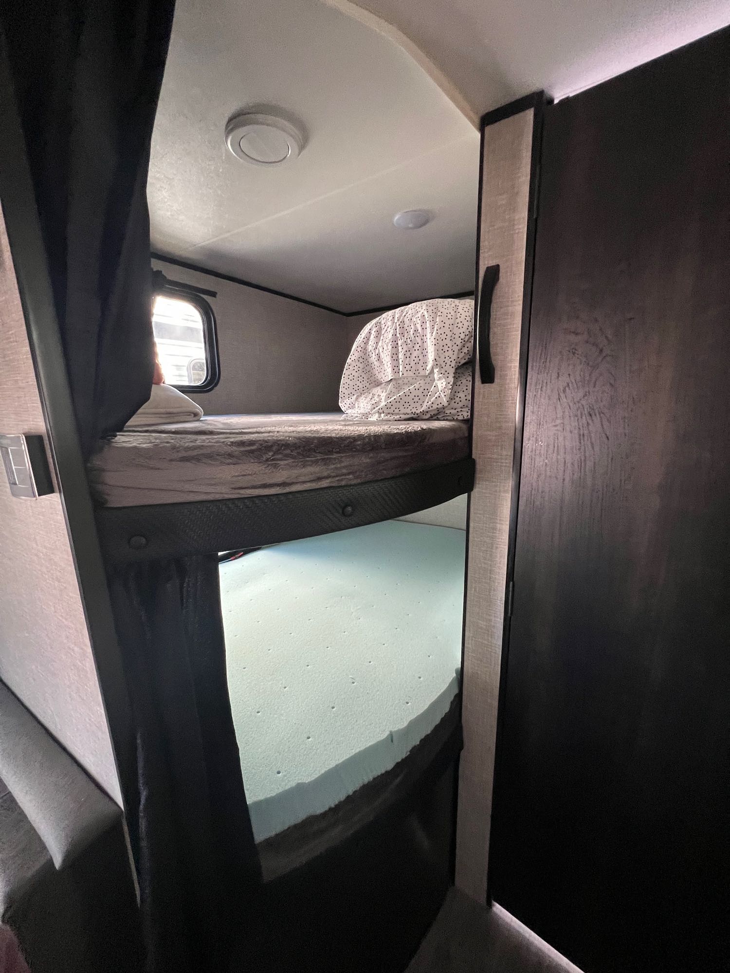Cozy bunk beds inside an RV rental. Top bunk has bedding; bottom bunk shows a light blue foam mattress, with a window nearby.. Jayco Jay Flight SLX 2022