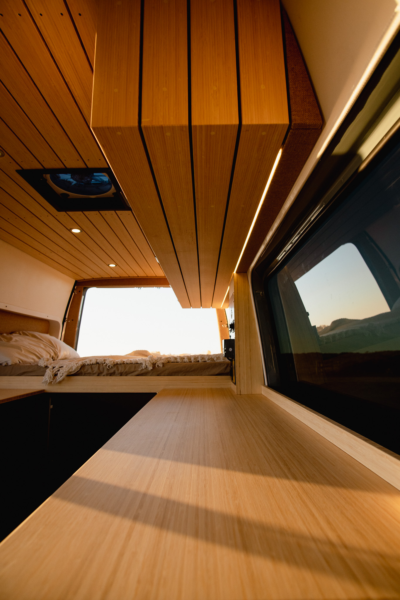 Cozy RV rental interior: light wood paneling, ambient LED lighting, and a comfortable bed for your next van adventure.. Mercedes-Benz Sprinter 2022