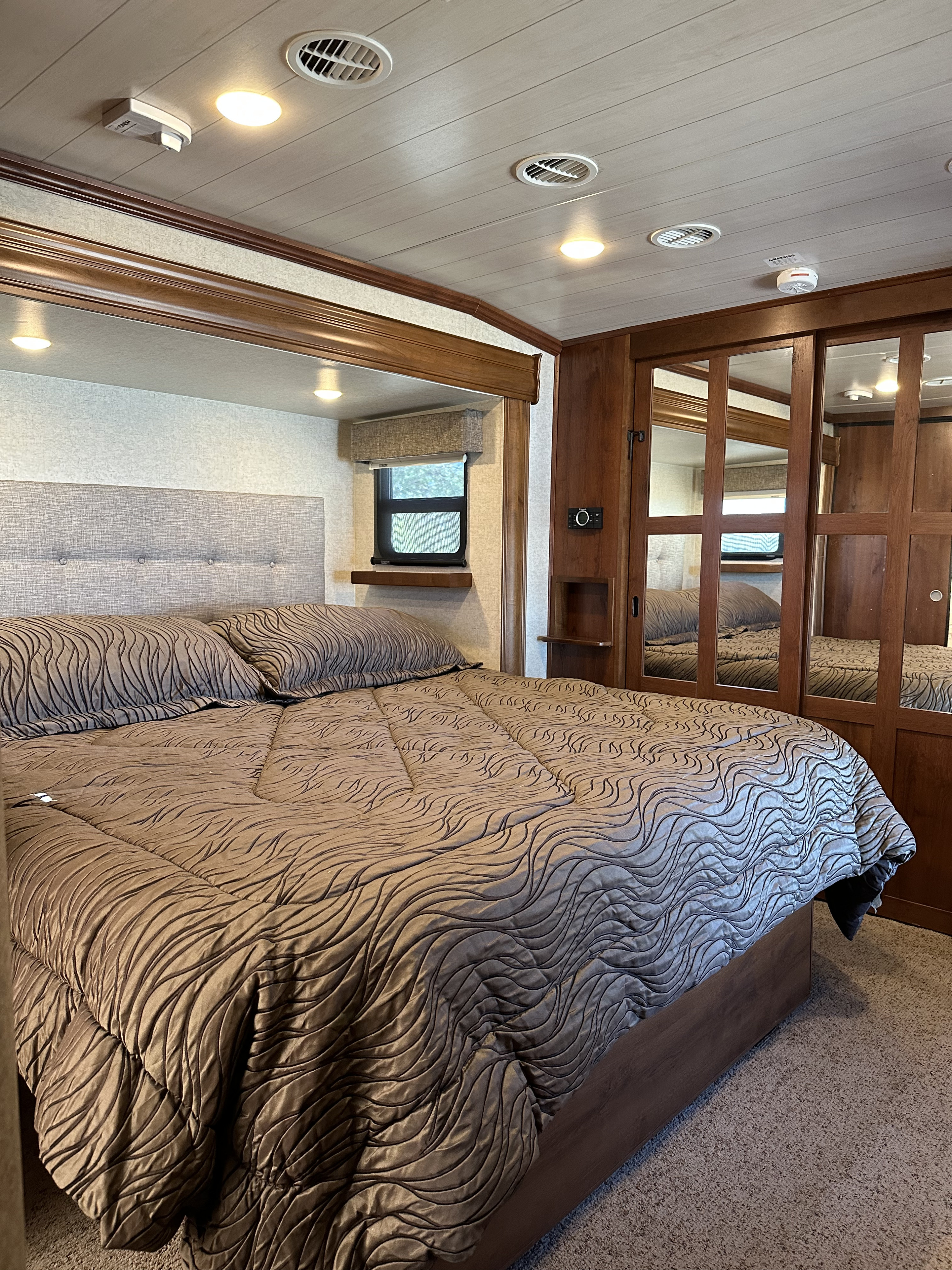 Cozy RV rental bedroom featuring a large bed, textured headboard, window, and mirrored closet.. Heartland Bighorn 2017