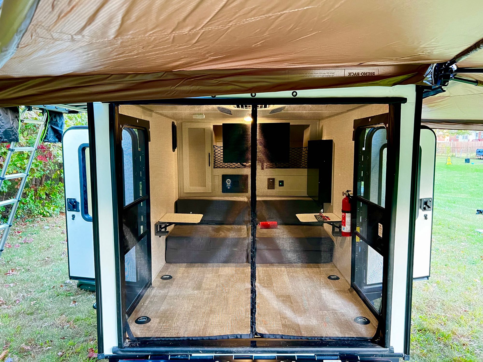 RV rental interior from rear, showing convertible beds, tables, fire extinguisher, and a screen door. Ready for outdoor living.. Forest River No Boundaries 2023