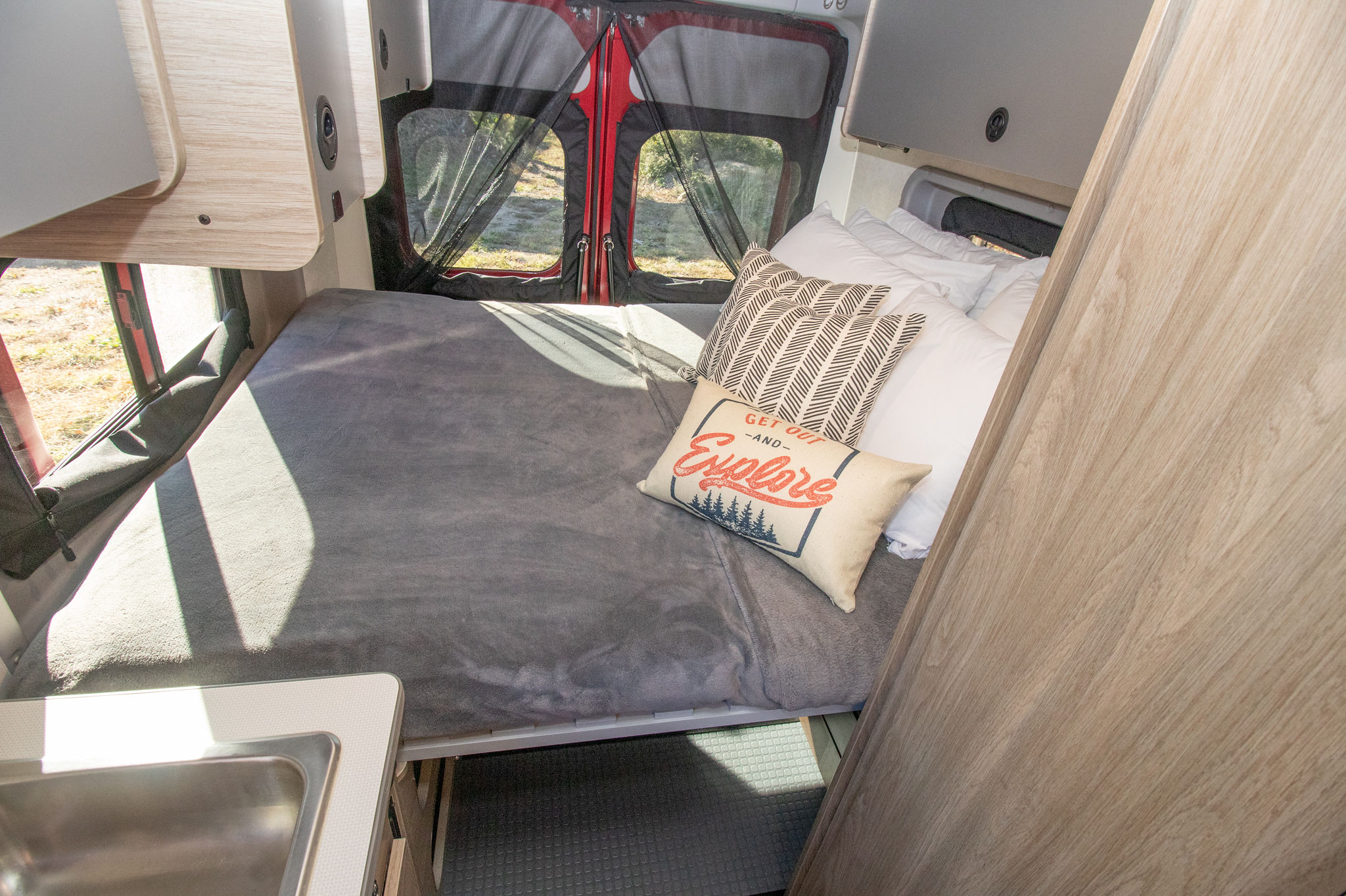 Inside an RV rental: a compact, comfortable bedroom with overhead storage, decorative pillows, and a nearby sink.. Winnebago Other 2022