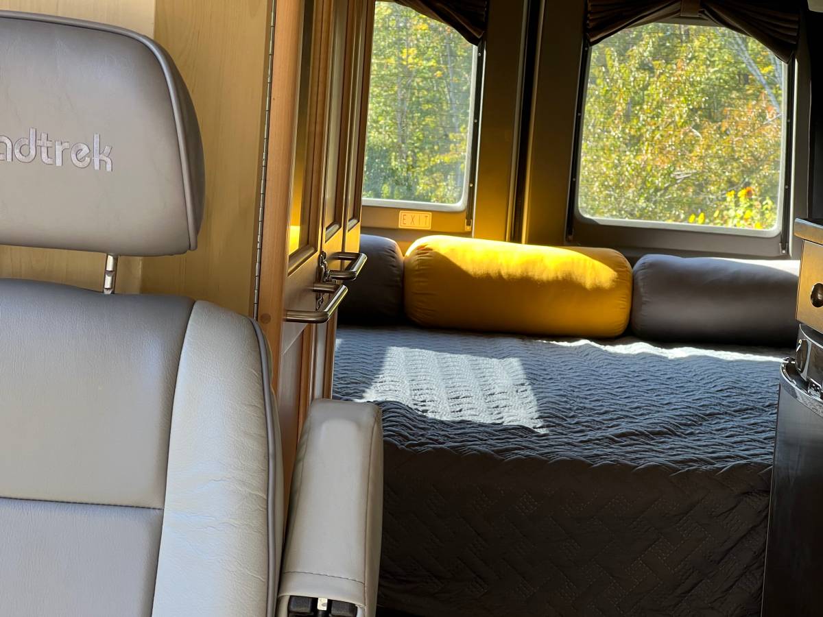 Inside this Roadtrek RV rental: comfy bed, bright windows showcasing nature, and a passenger seat in the foreground.. Roadtrek Roadtrek Class B 2006