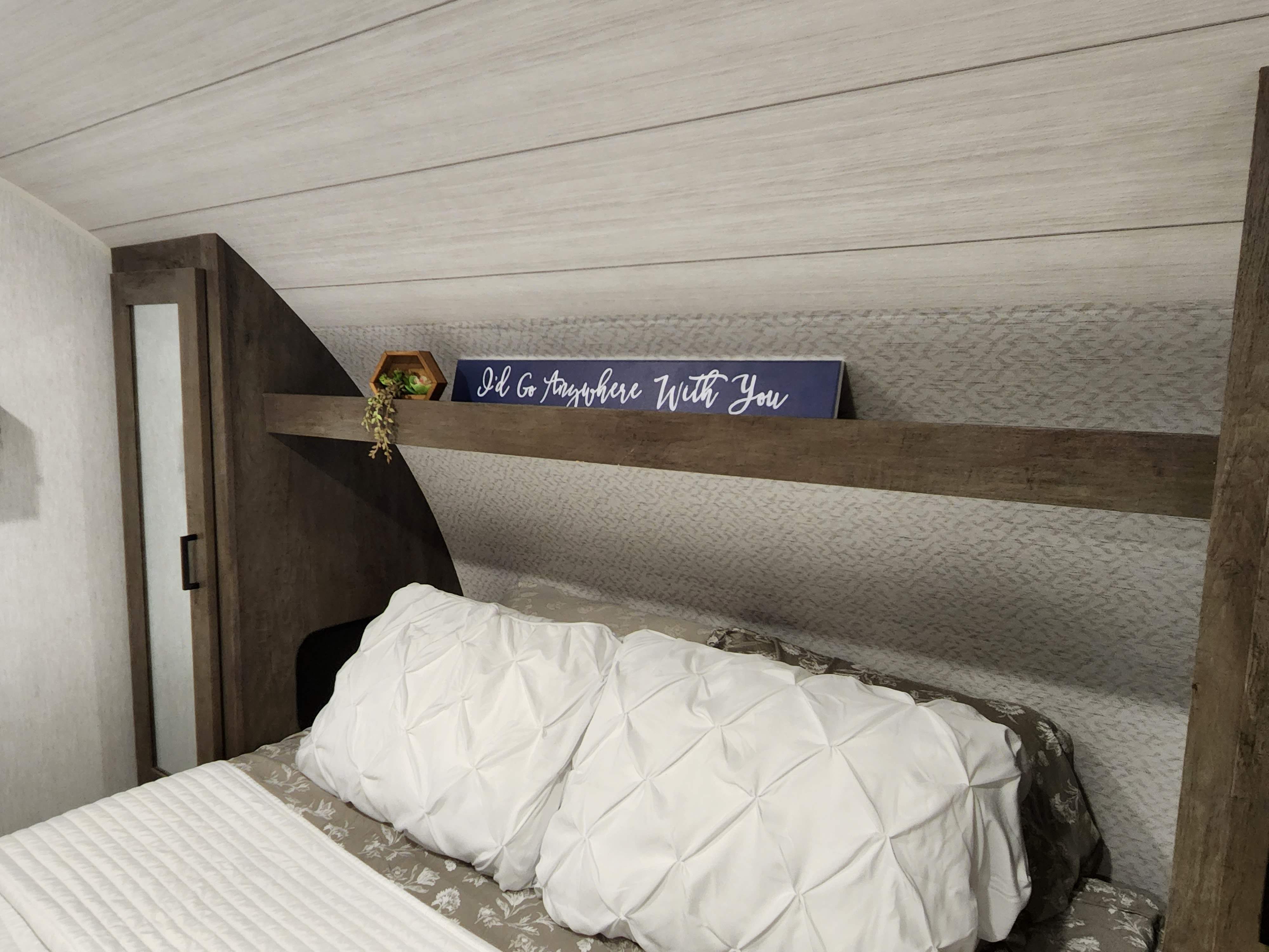 Comfortable RV rental bedroom featuring a cozy bed, decorative shelf with a sign, and stylish wood-look finishes.. Forest River Salem Cruise Lite 2022