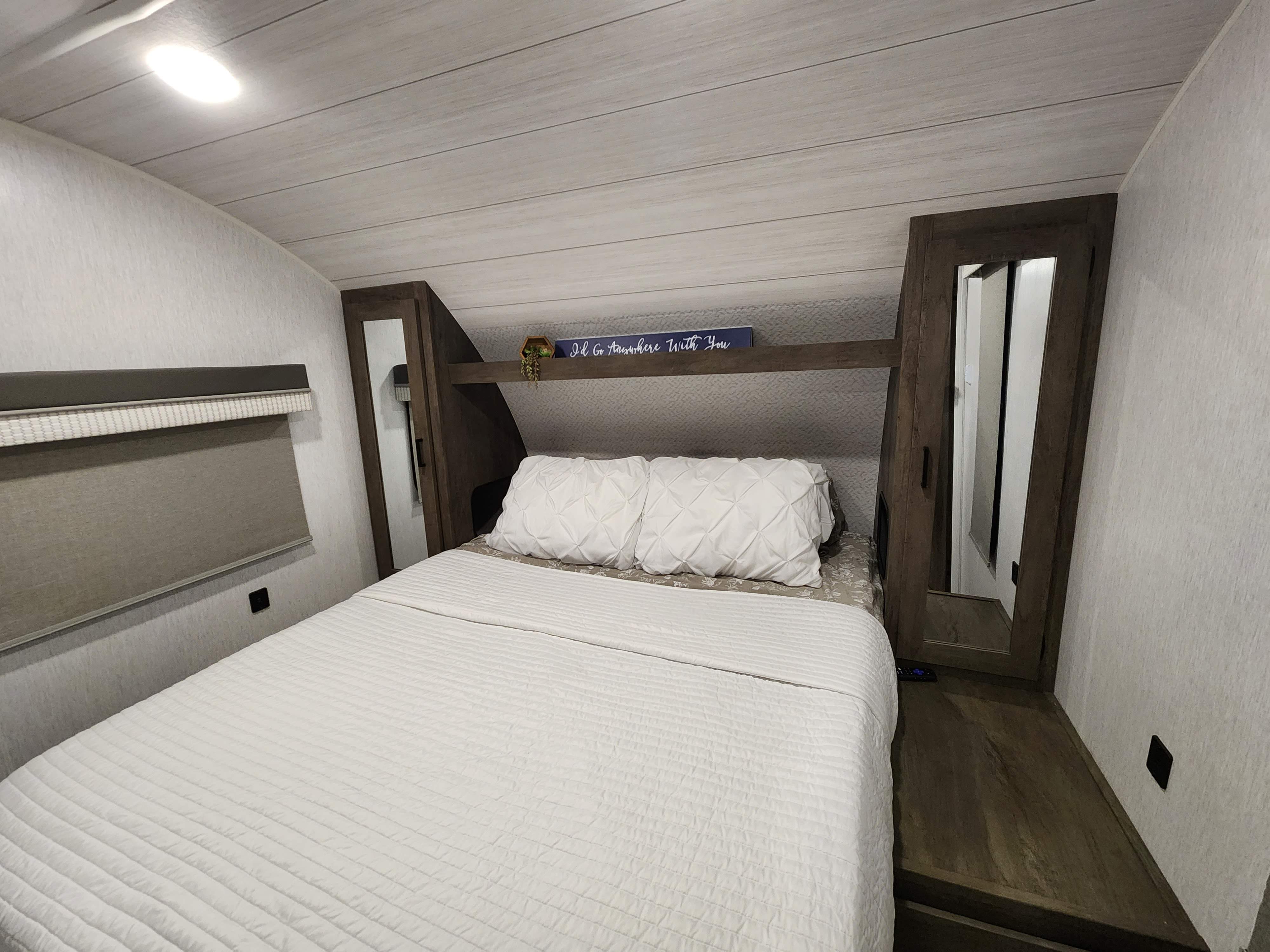 Cozy RV rental bedroom featuring a comfortable bed with white bedding, overhead shelf, window shade, and mirrored wardrobes.. Forest River Salem Cruise Lite 2022