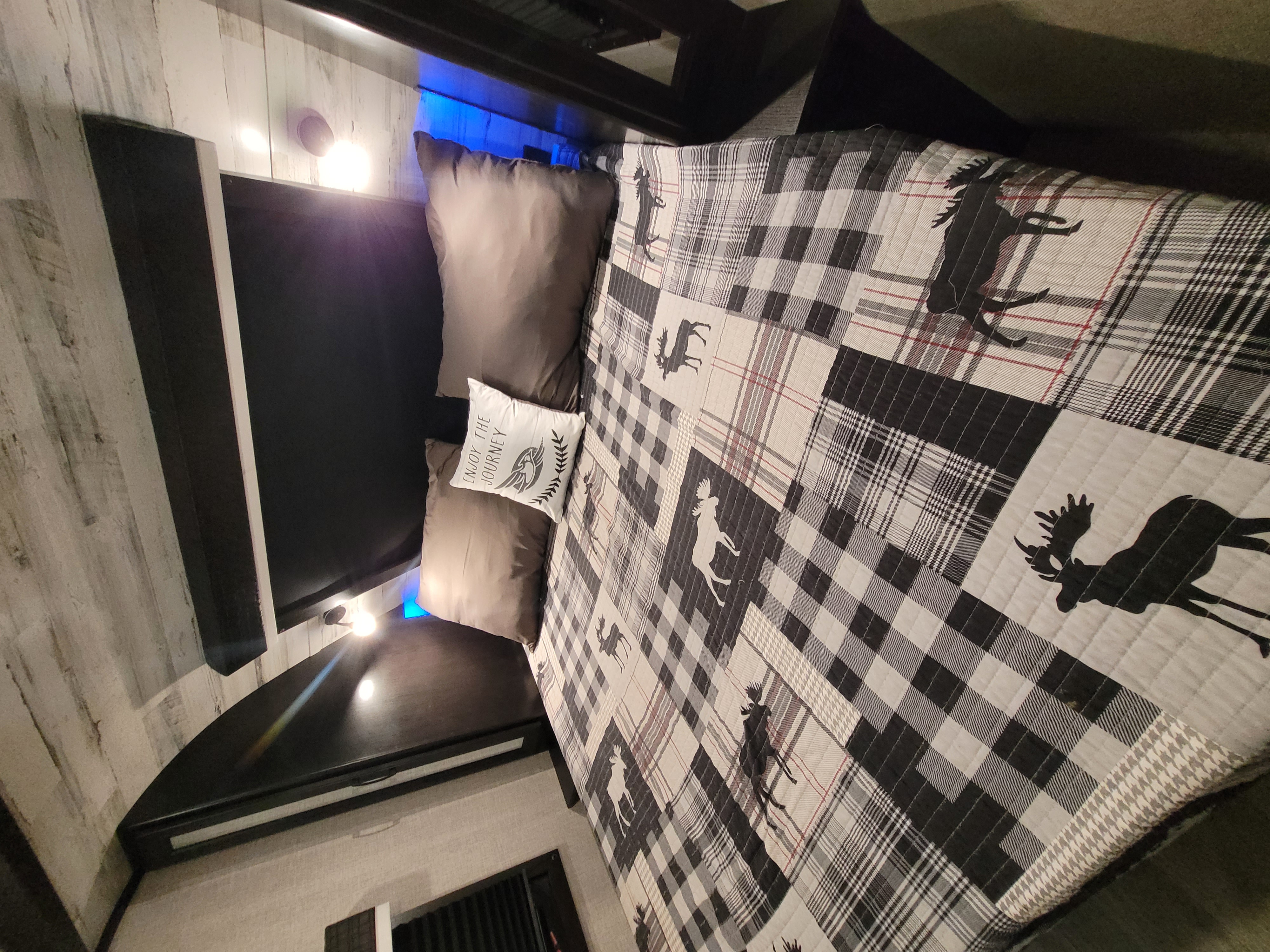 Cozy RV rental bedroom with plaid and moose-themed quilt, pillows, and ambient blue lighting.. Jayco White Hawk 2022