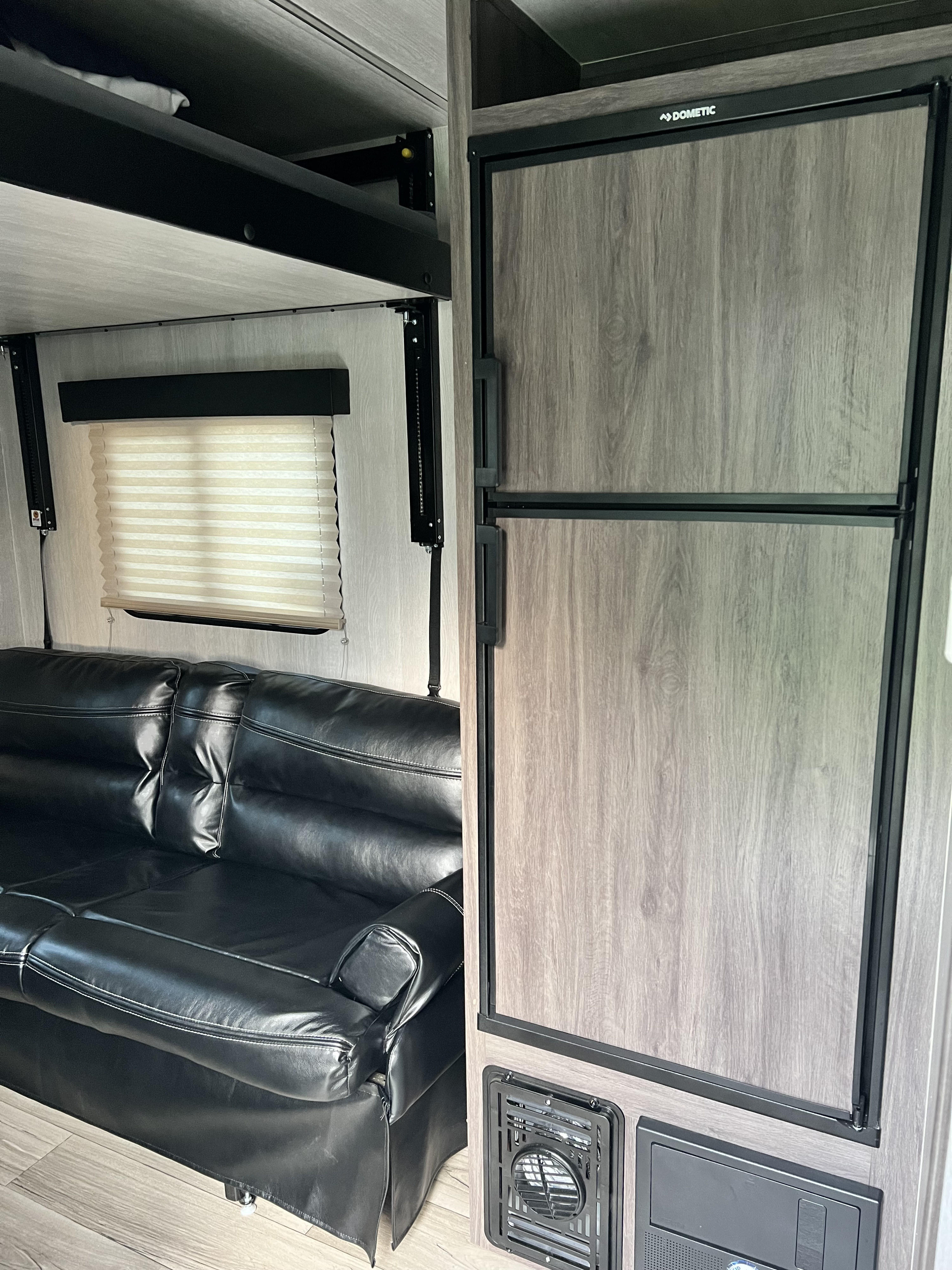 Spacious RV rental interior featuring a black leather sofa, Dometic refrigerator, and overhead lift bed system.. Genesis Supreme Rv Genesis Supreme 2023