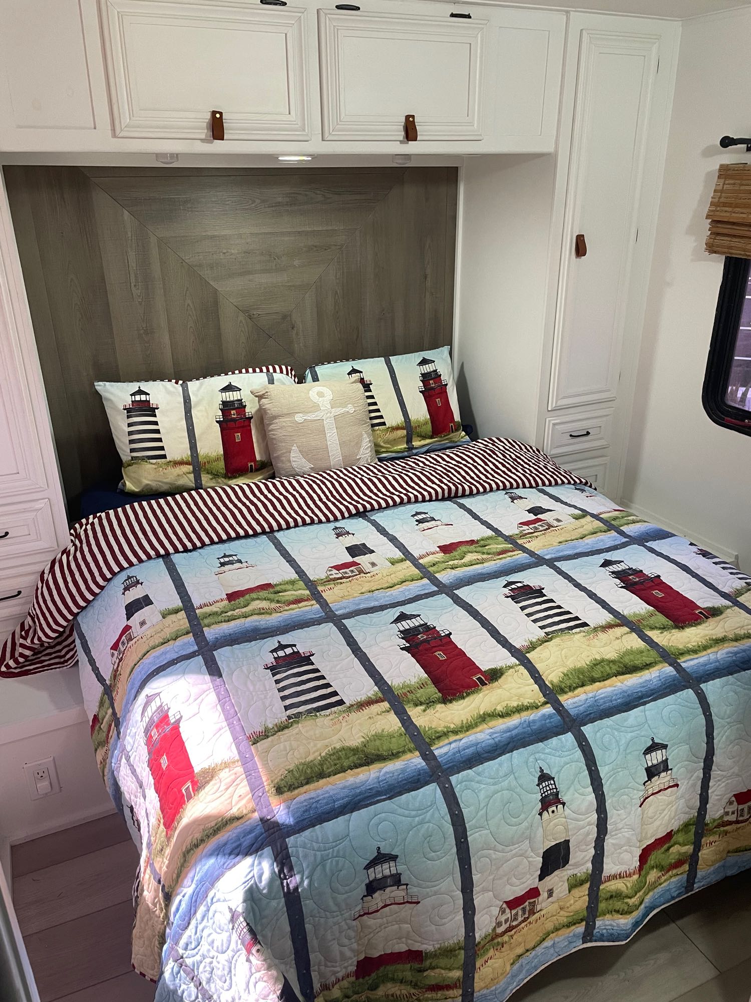 Cozy RV rental bedroom with a lighthouse quilt, white cabinets, and wood-paneled headboard, perfect for a relaxing travel escape.. Gulf Stream Independence 2006